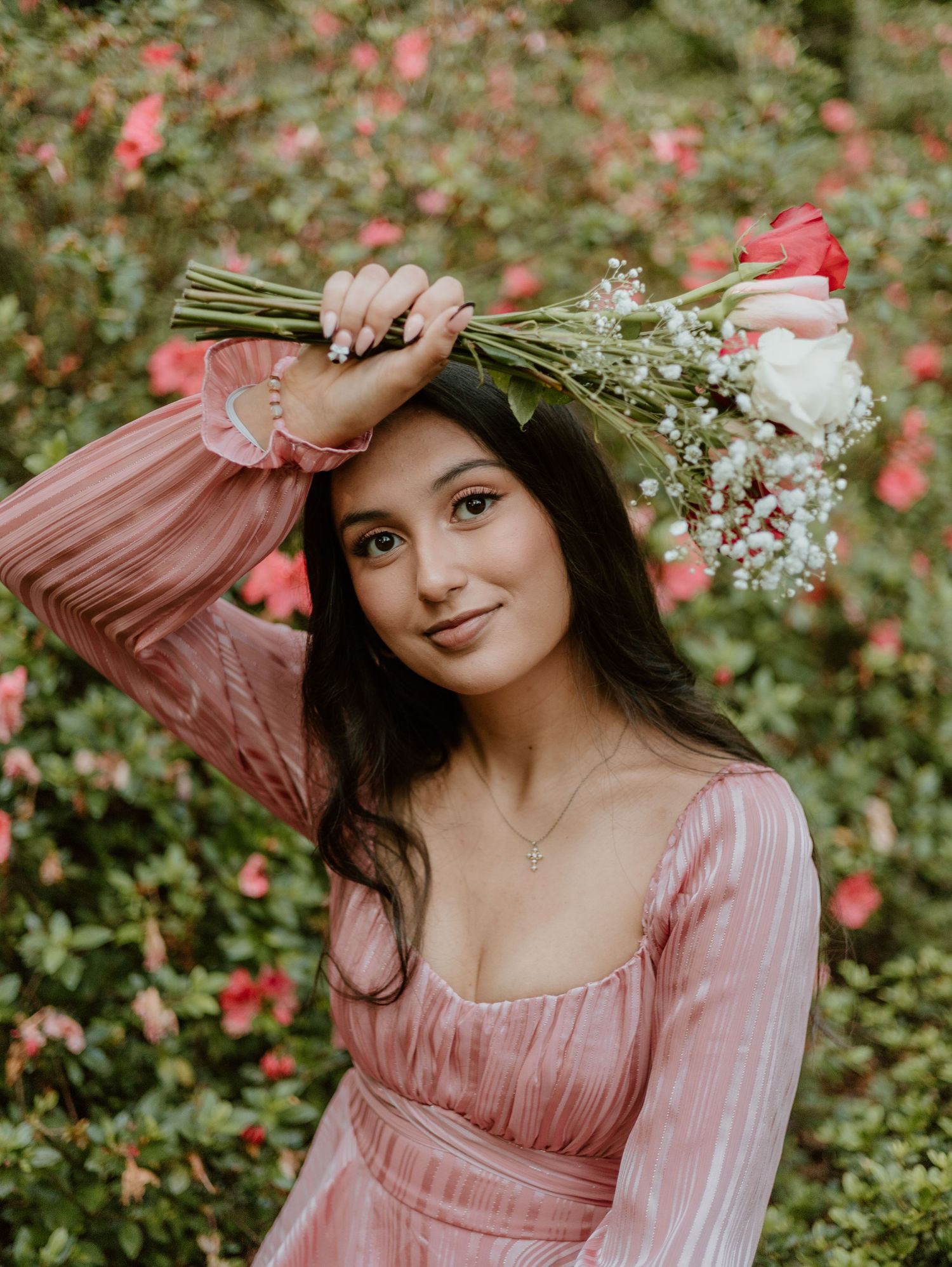 Portrait of person in pink vintage dress holding flowers in garden setting.