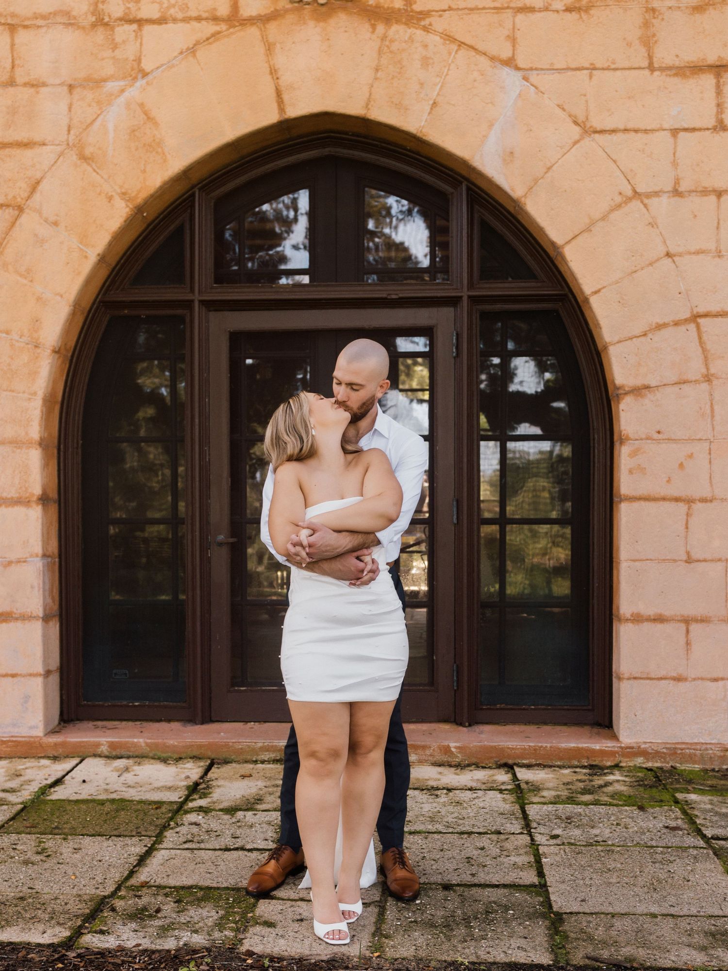 A couple shares an intimate moment in front of an arched stone doorway.
