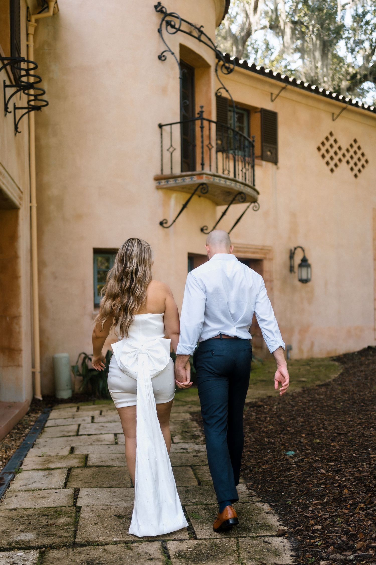 Couple walking together on stone pathway outside Spanish colonial style building.