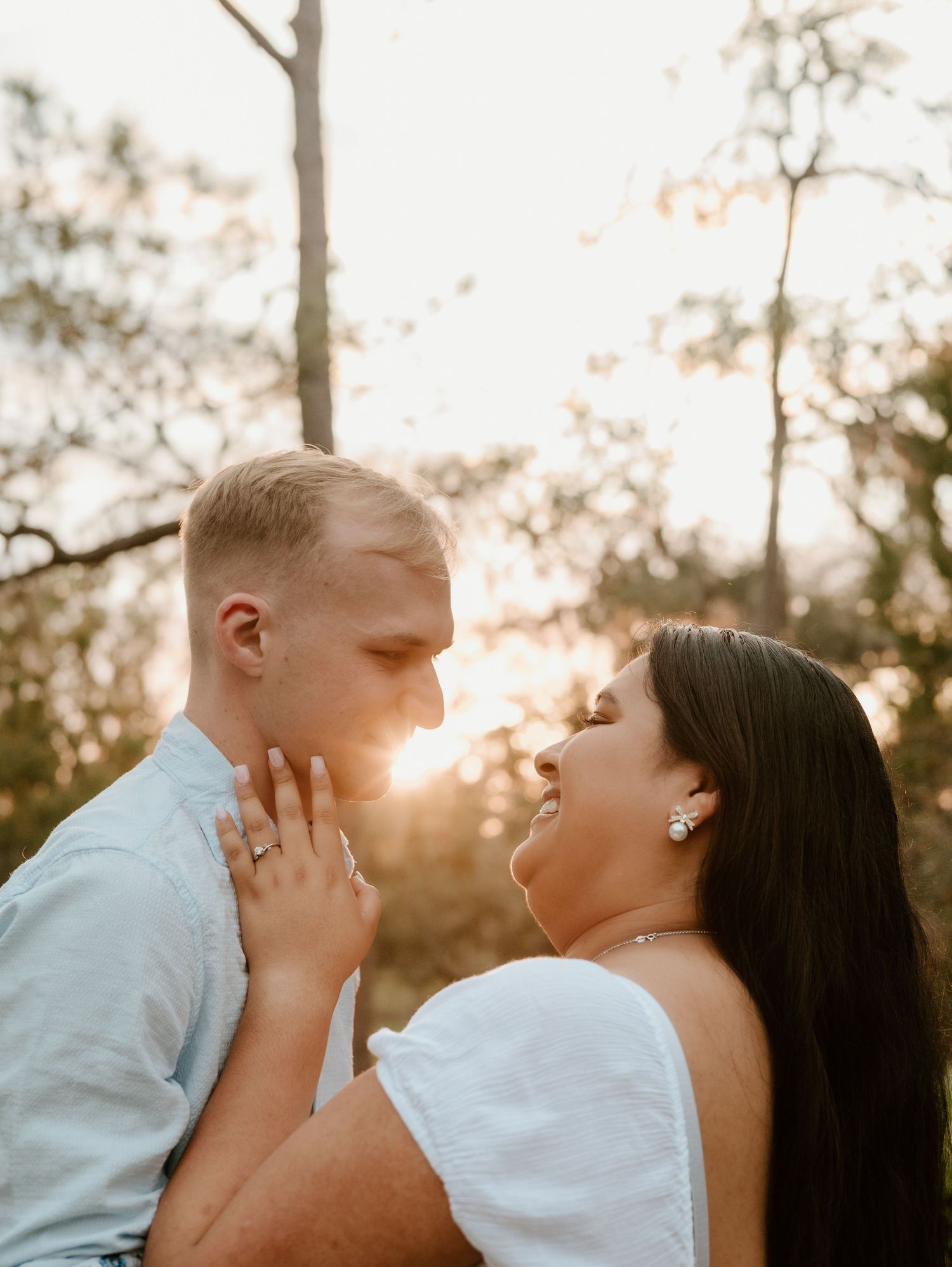 Intimate sunset engagement photo with golden light filtering through trees.