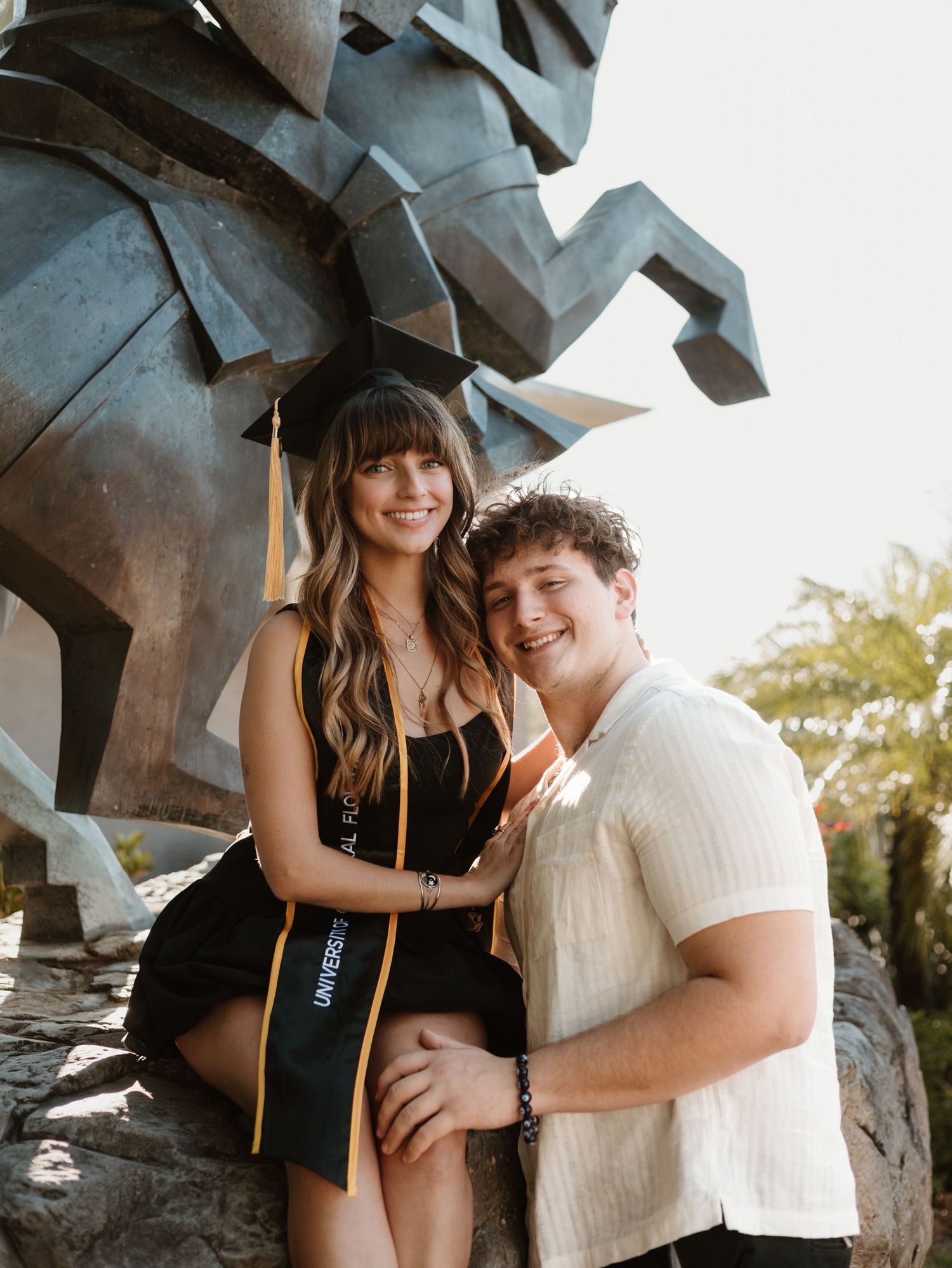 Couple posing together by modern geometric sculpture outdoors.