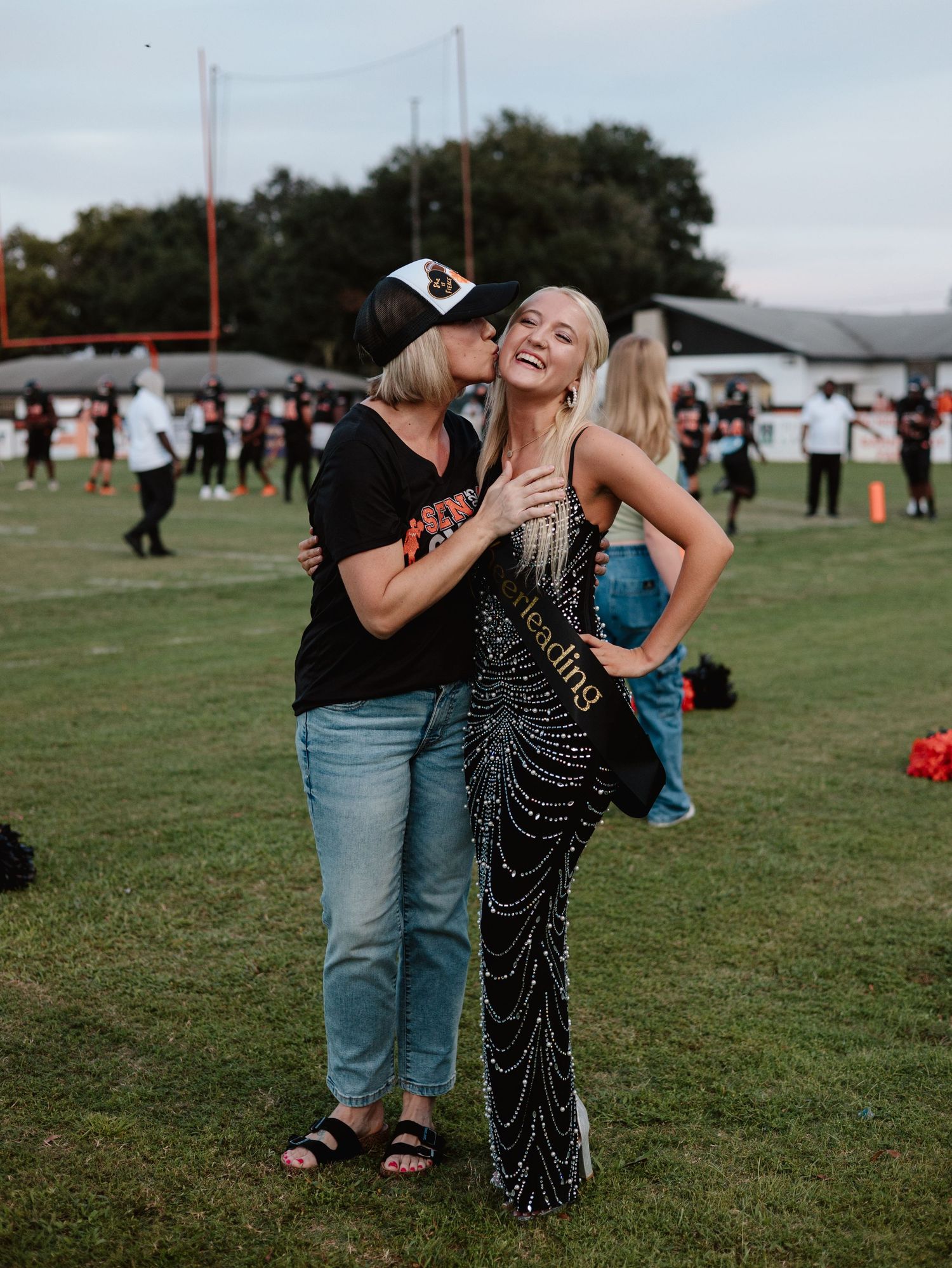 A candid moment of laughter and celebration on a sports field during an event with a sparkly gown.
