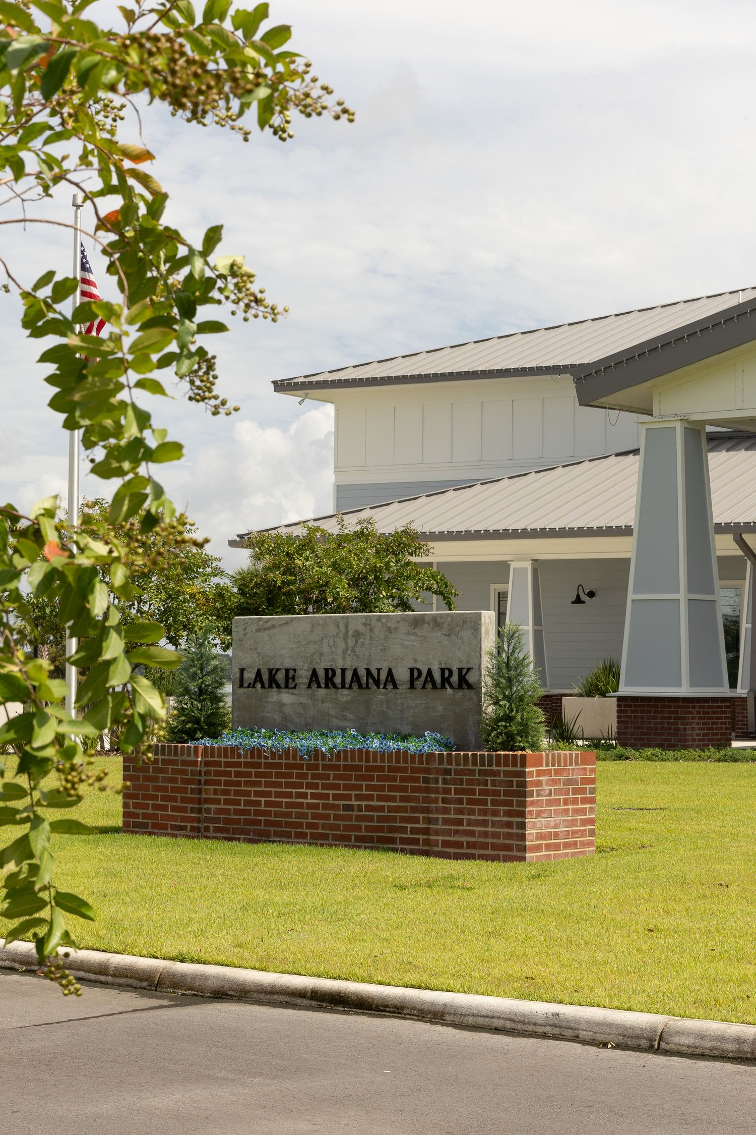 Lake Ariana Park entrance sign on brick planter with American flag and white building in Auburndale, Florida.