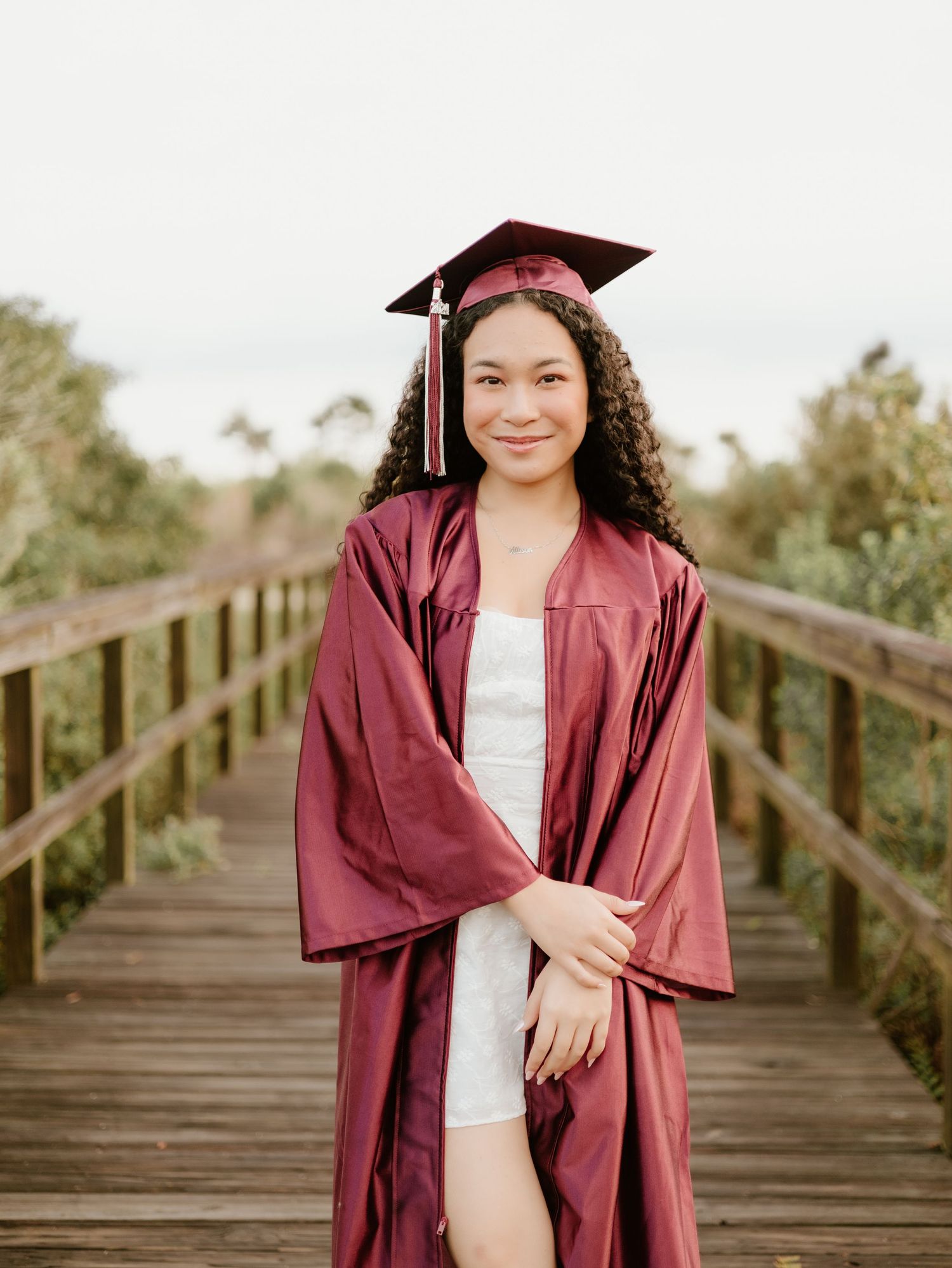 Graduation photos on wooden boardwalk wearing maroon cap and gown.