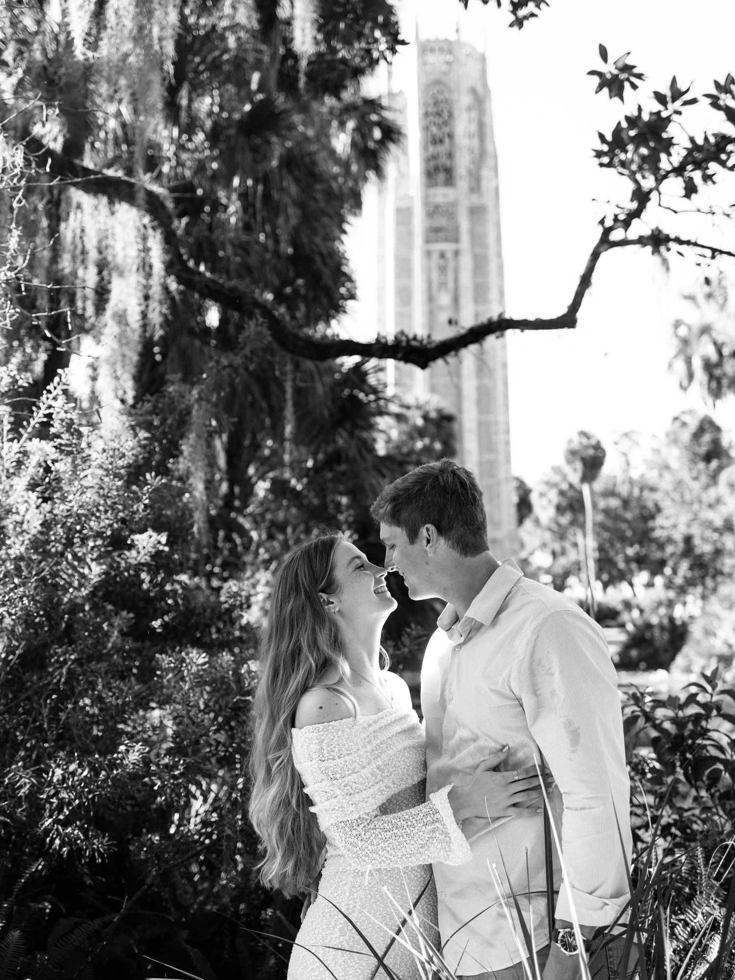 A romantic couple shares tender moments in a garden setting captured in black and white photography.