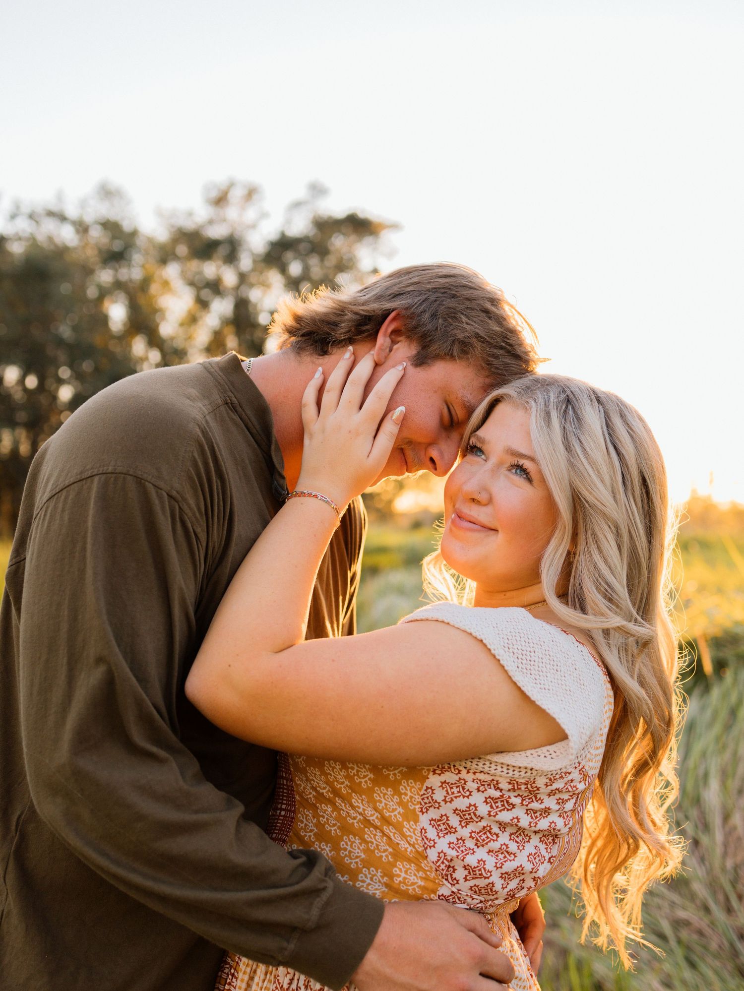 A romantic couple embraces in a golden field during sunset, creating a tender moment in warm lighting.