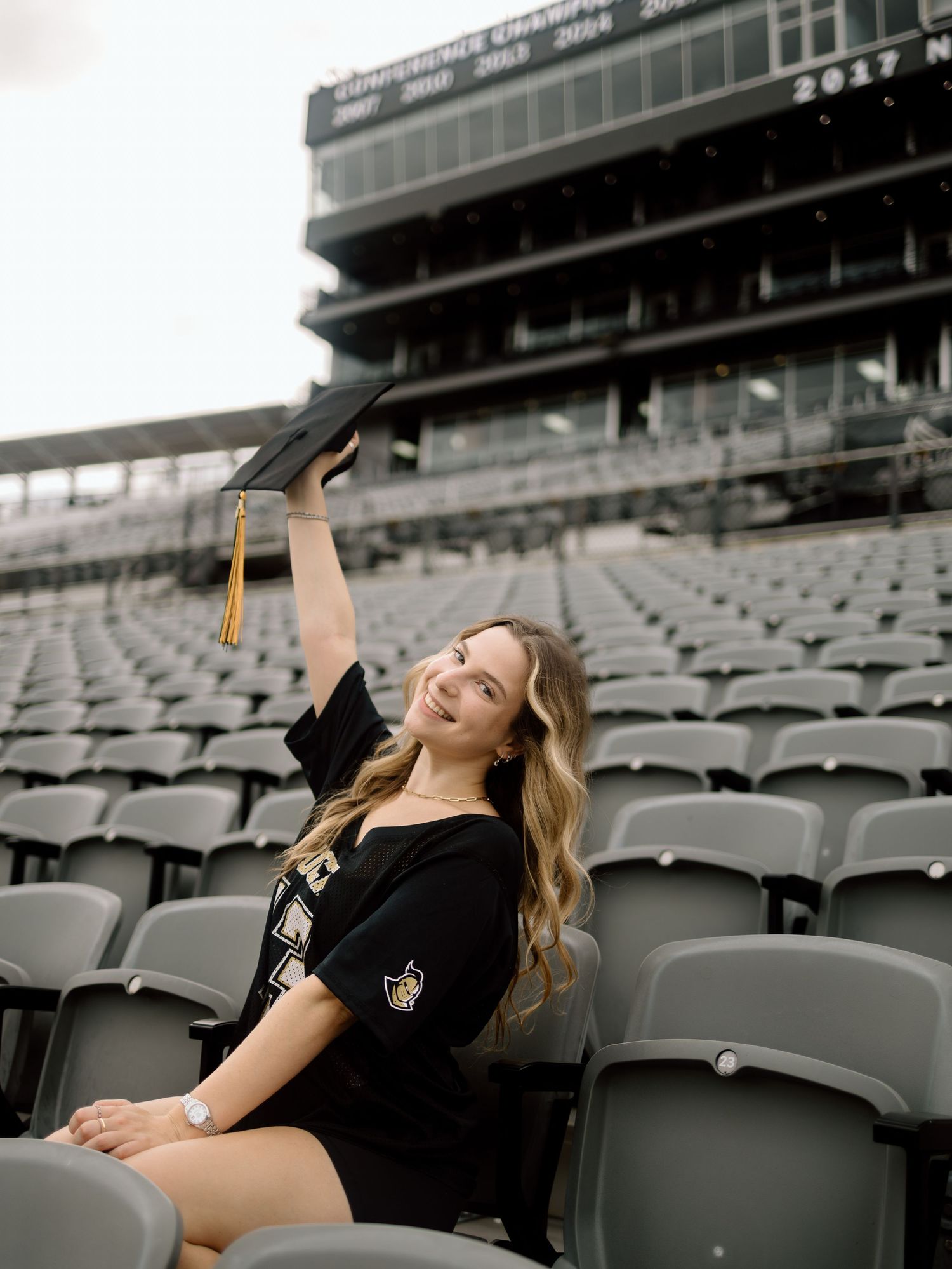 A person in a black outfit lounges across empty stadium seats while striking dramatic poses in black and white.