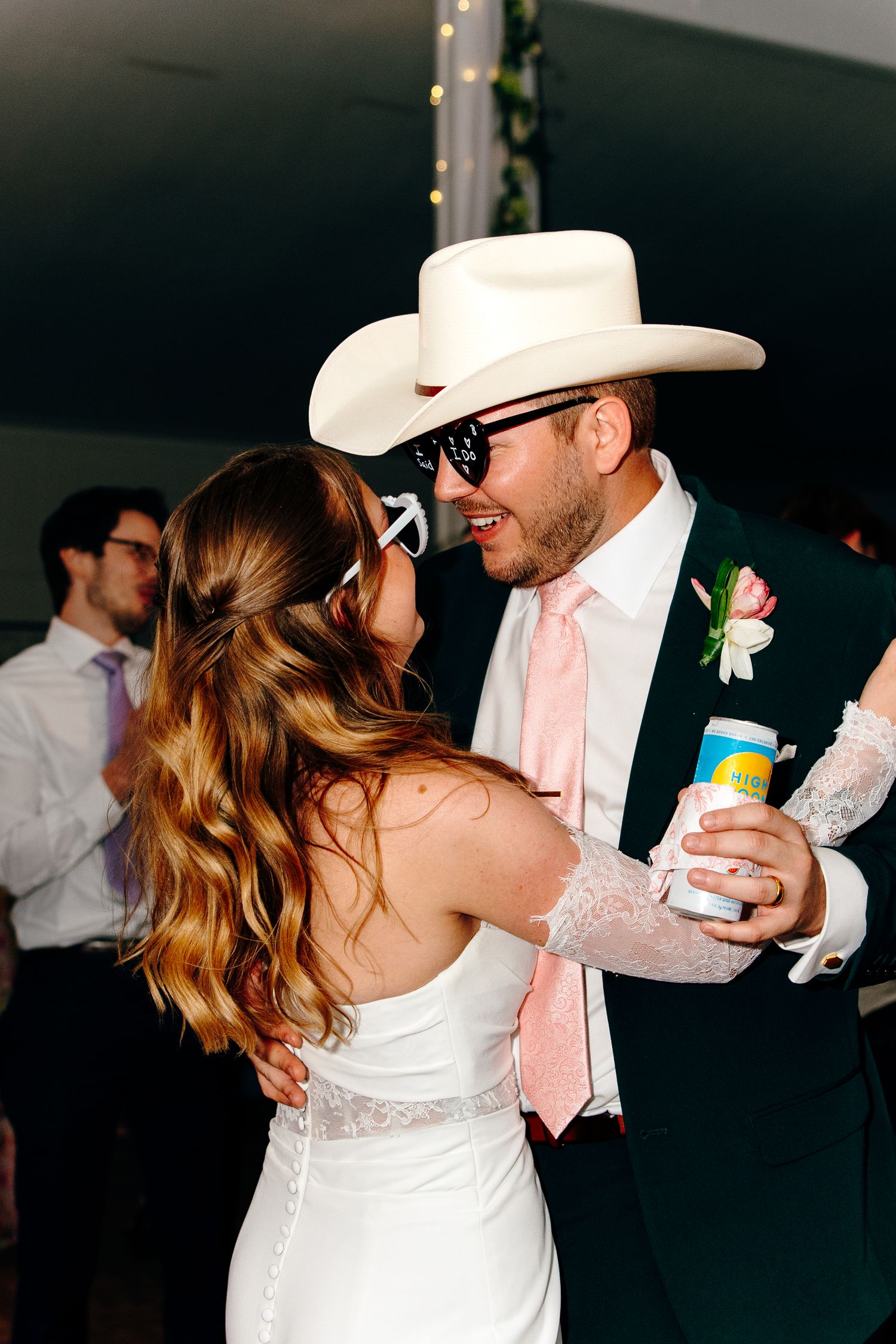 Bride and groom sharing a dance at wedding reception, groom wearing white cowboy hat and pink tie.