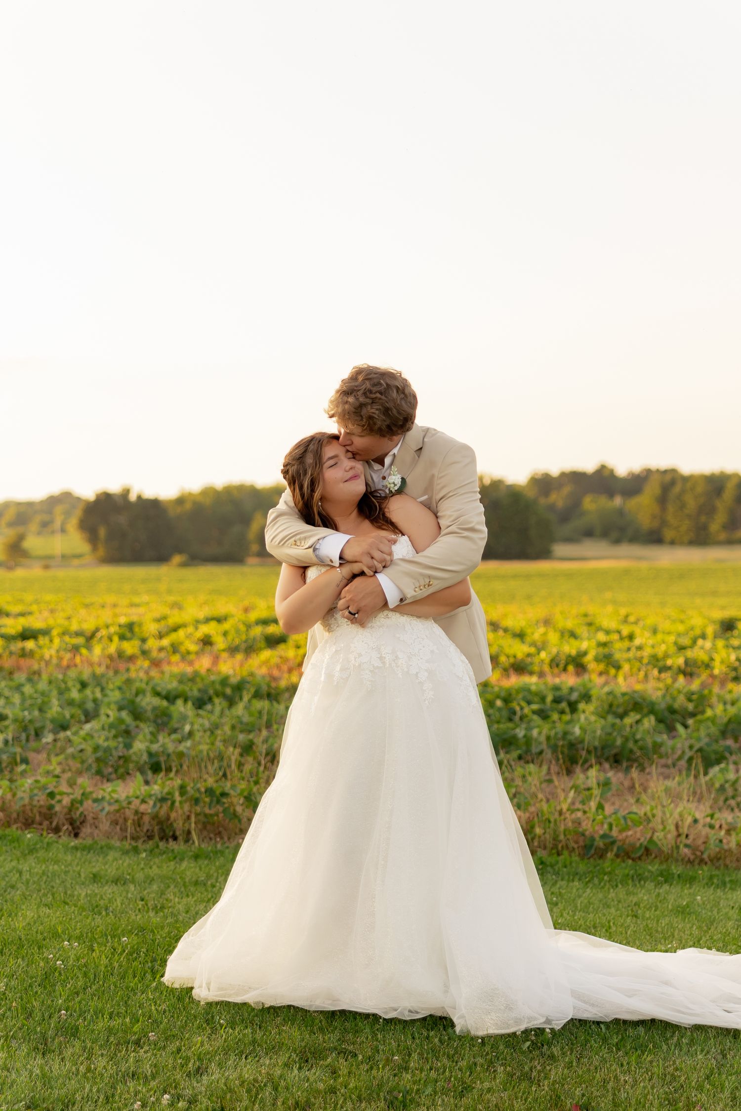 Bride and groom embracing in a romantic kiss at sunset with a lush vineyard in the background on their wedding day.