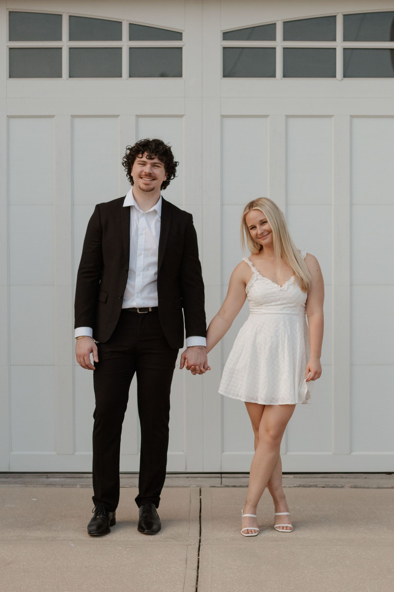 Creative engagement photos showing contrasting heights against white garage doors.