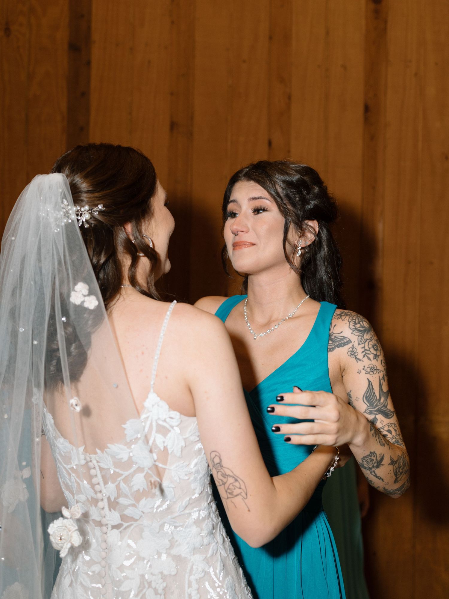 A bride in a lace wedding dress dances with a bridesmaid wearing a turquoise gown at an indoor venue.