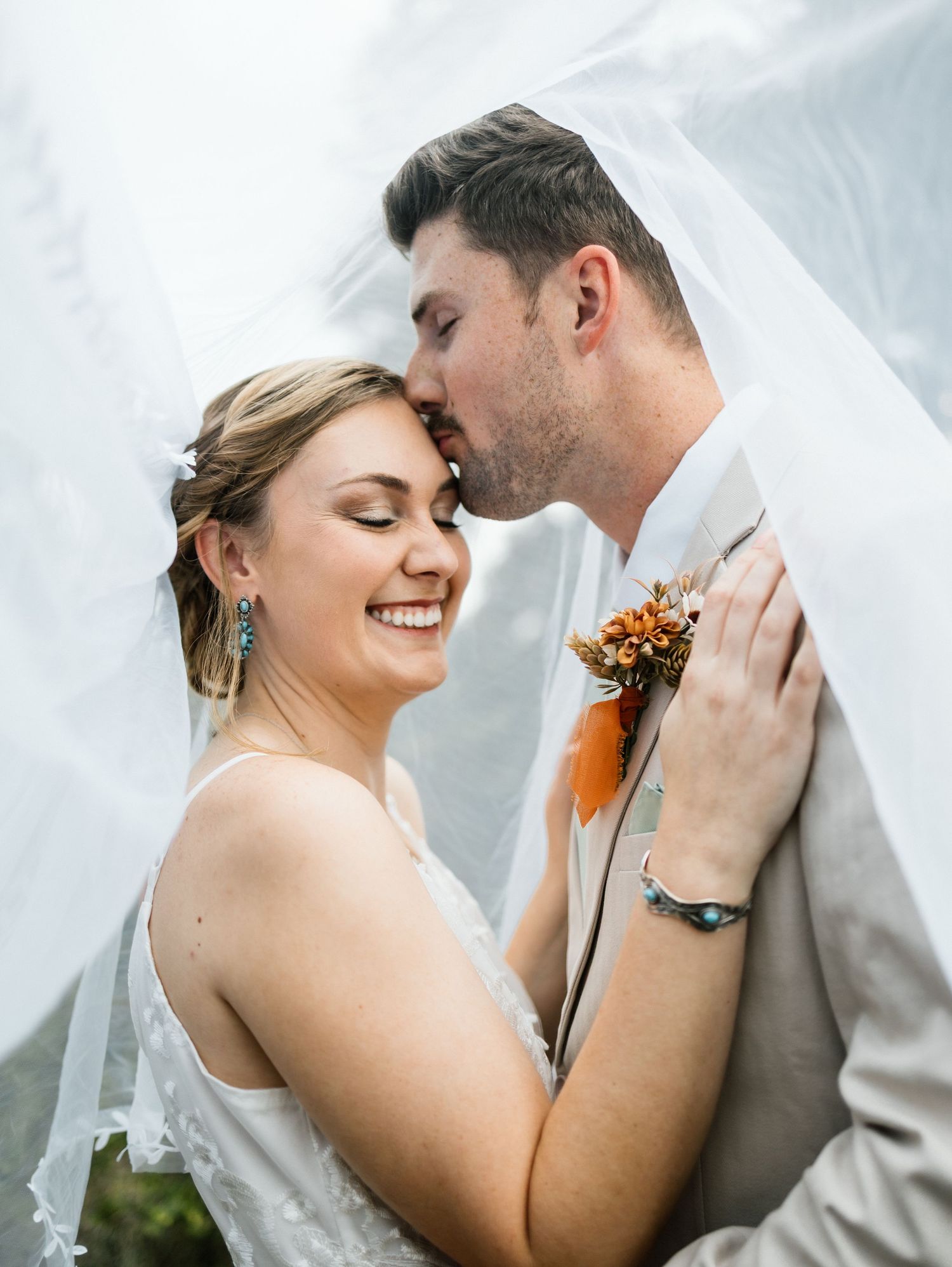 Romantic wedding couple shares intimate moments together in a series of delicate poses beneath flowing white veil.
