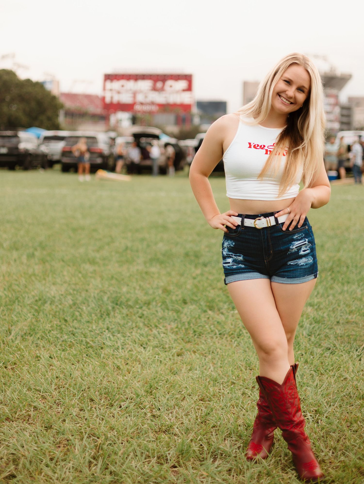 Person in denim shorts and red boots standing casually in a grassy field.