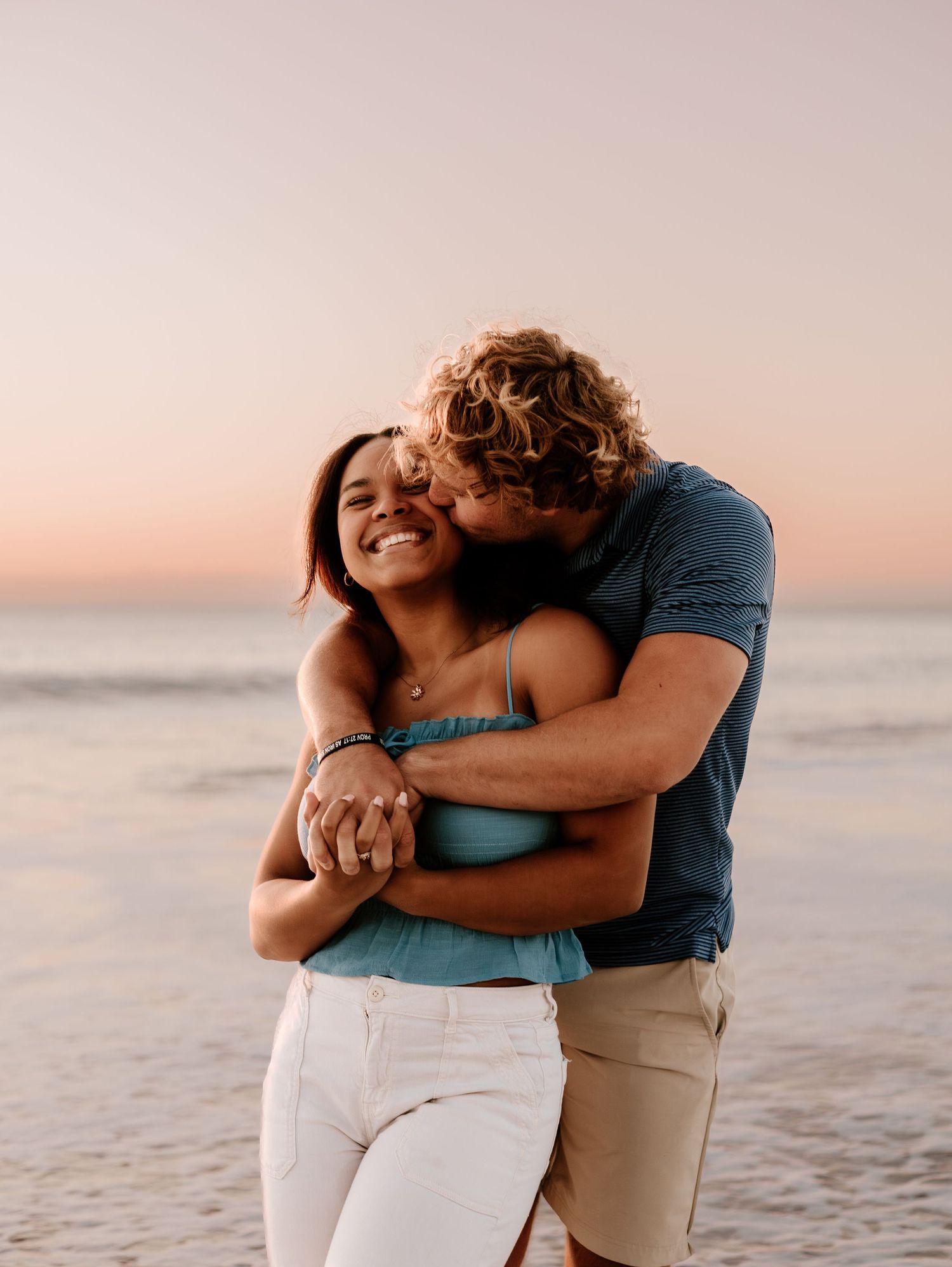 Couple sharing tender moment while standing together on beach at sunset.