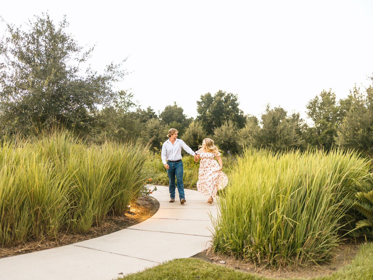 People walking along a winding concrete path through tall grasses and natural vegetation in a coastal park setting.