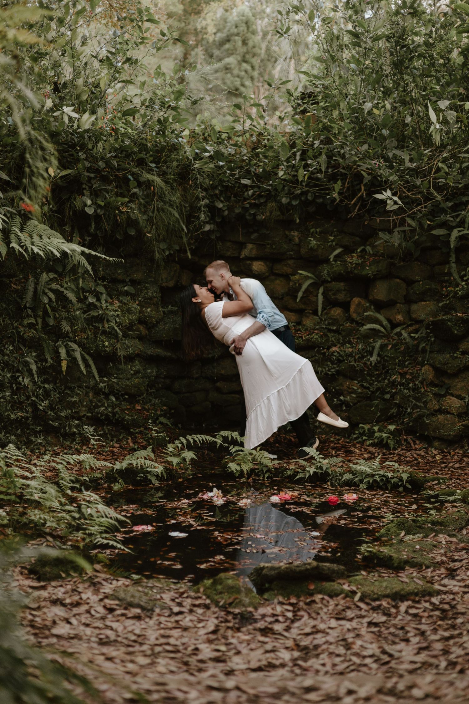 Romantic dip pose in a lush green garden setting with stream and fallen leaves.