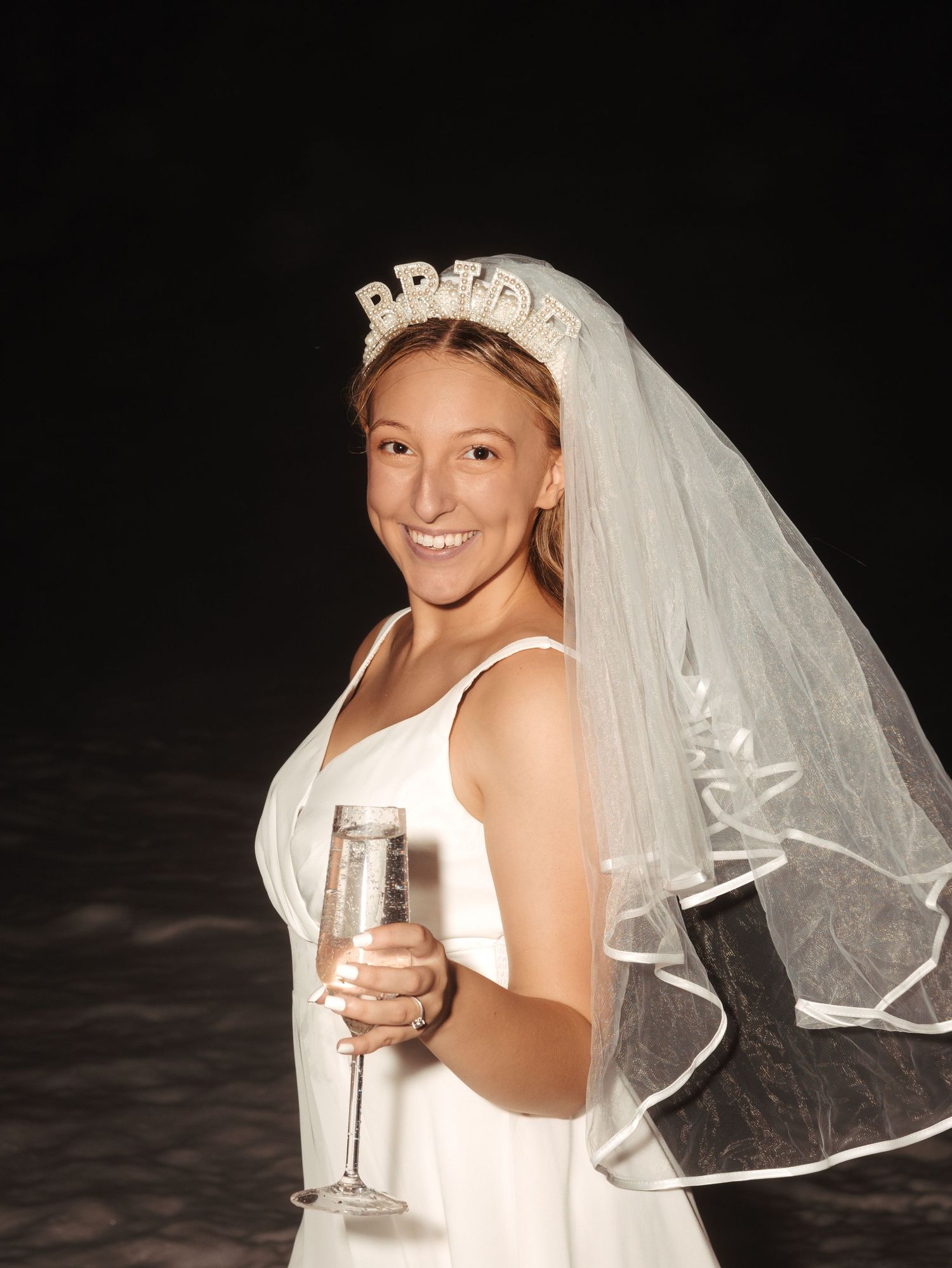 A bridal portrait series showing someone in a wedding veil and crown holding champagne.