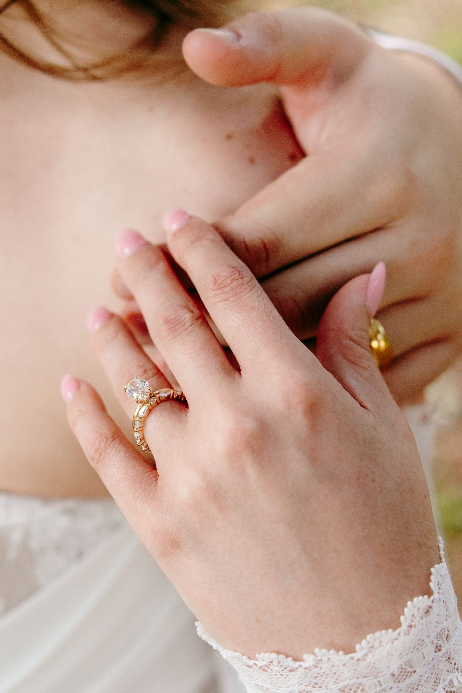 Close-up of a bride's hands wearing a gold diamond engagement ring with lace wedding dress sleeve.