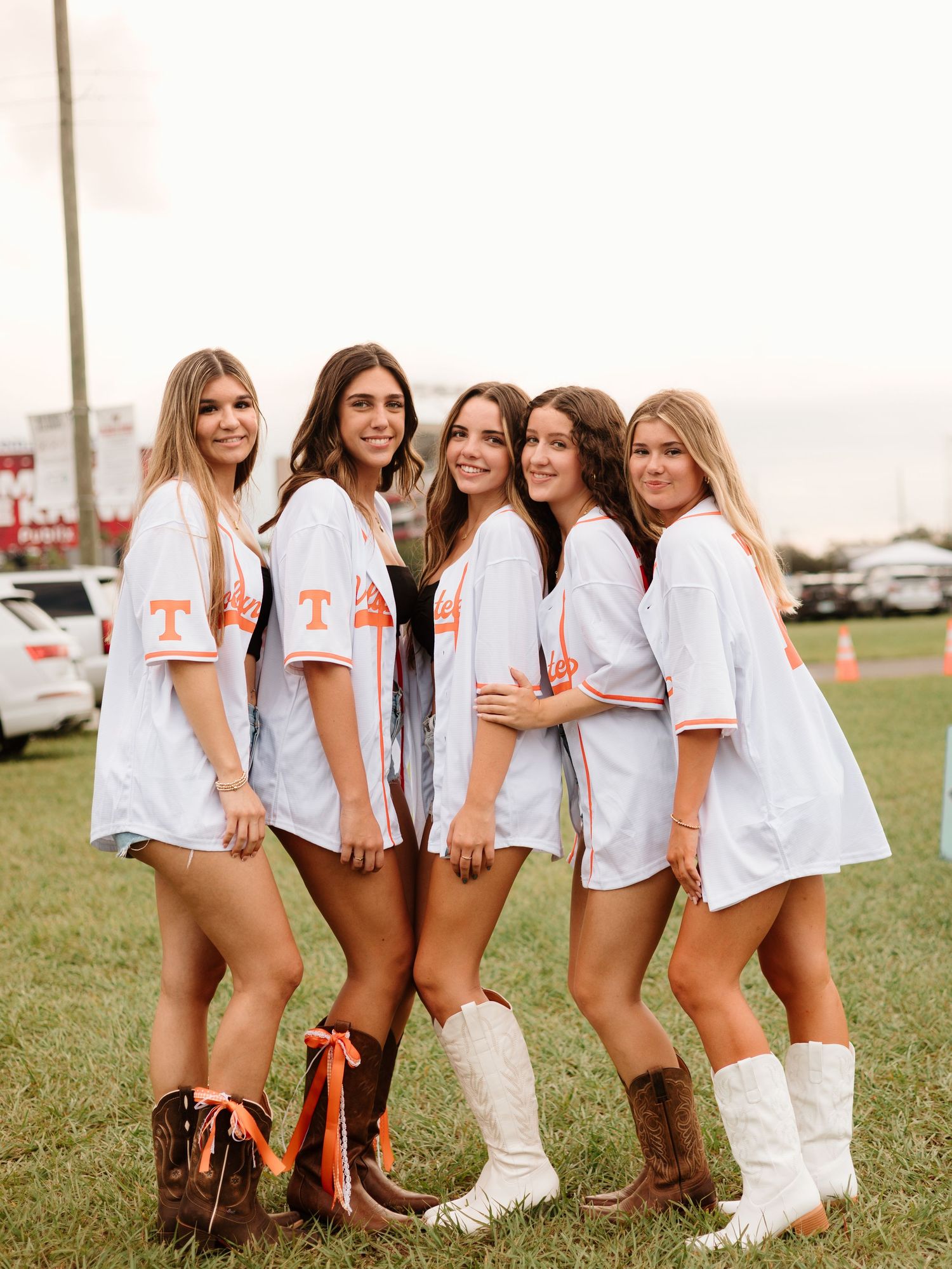 A line of teammates in white uniforms and cowboy boots pose together on grass during a sunny evening.