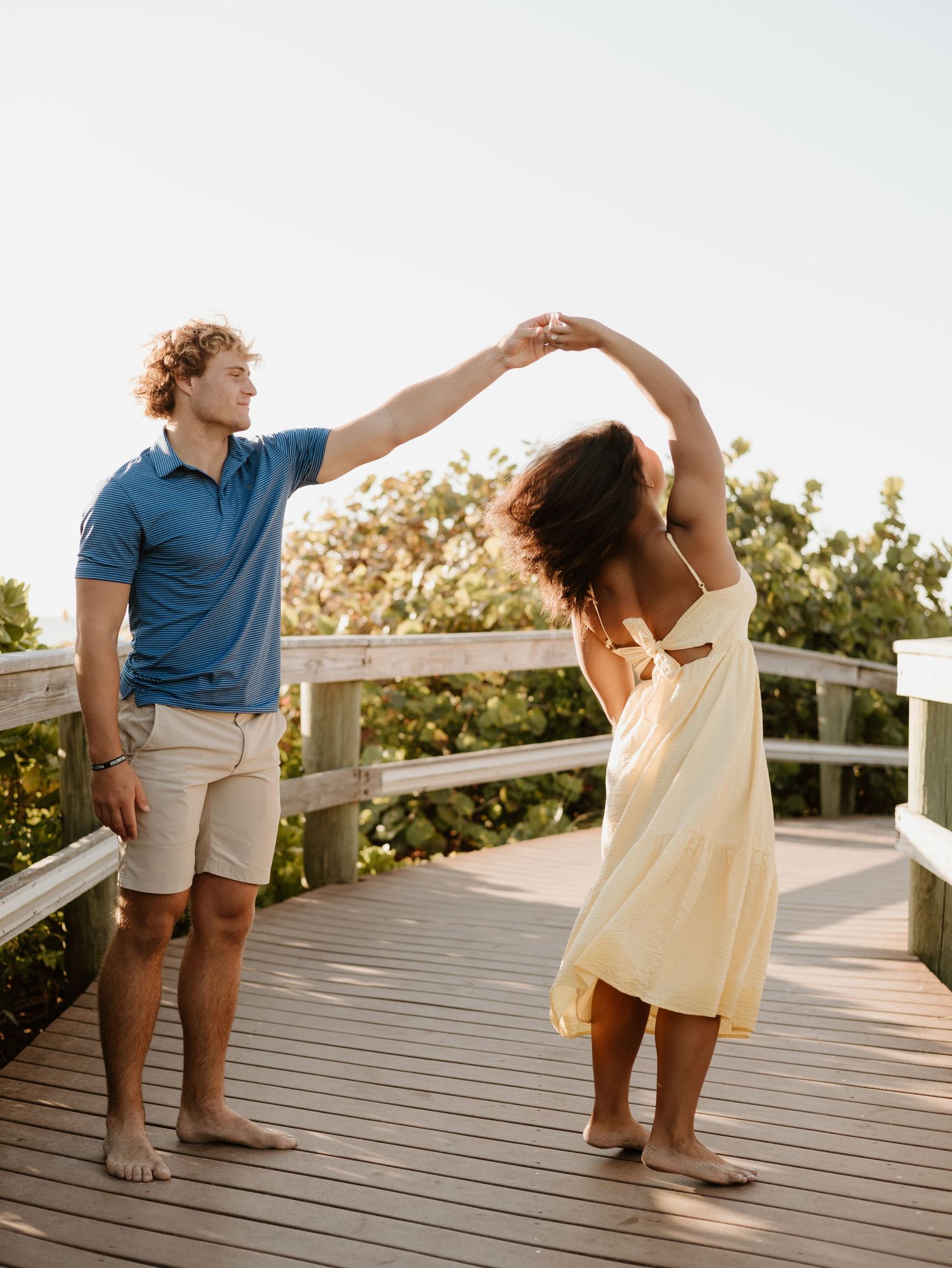 A couple dancing together on a wooden deck at sunset, with the woman twirling in a flowy cream dress.