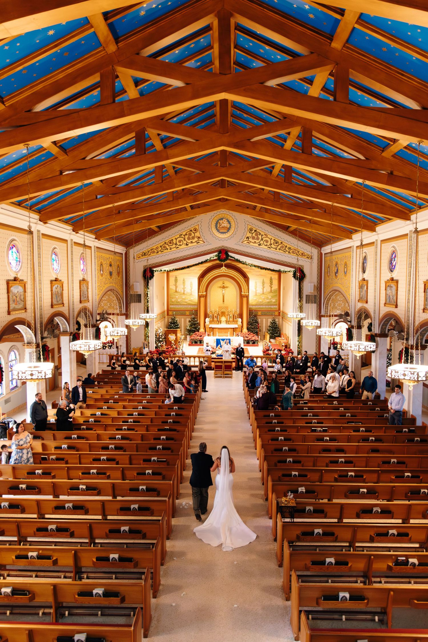Bride walks down the aisle of an ornate wooden church with vaulted ceilings during a wedding ceremony.