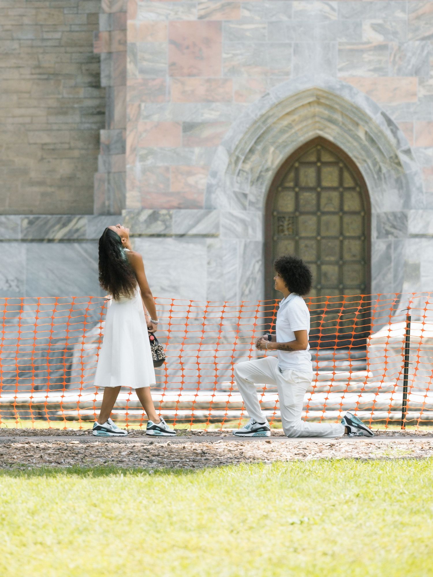 Two people in white clothing walk past a brick wall with Gothic arched doorways in a sequence of motion shots.