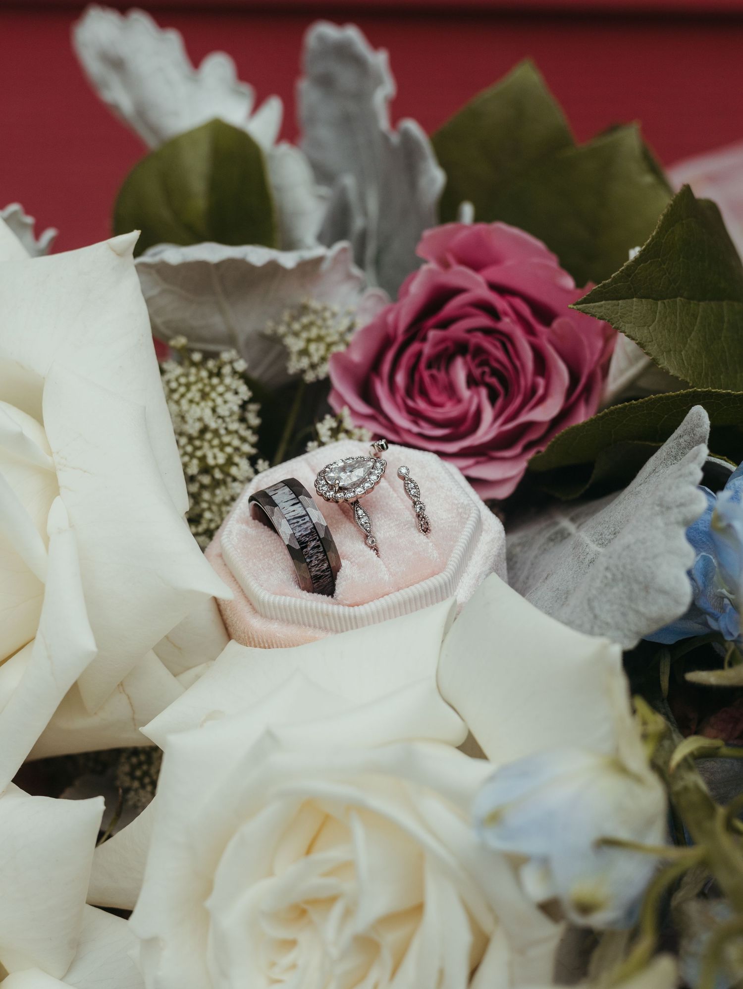 Wedding rings nestled in pink and white roses with delicate floral arrangement.
