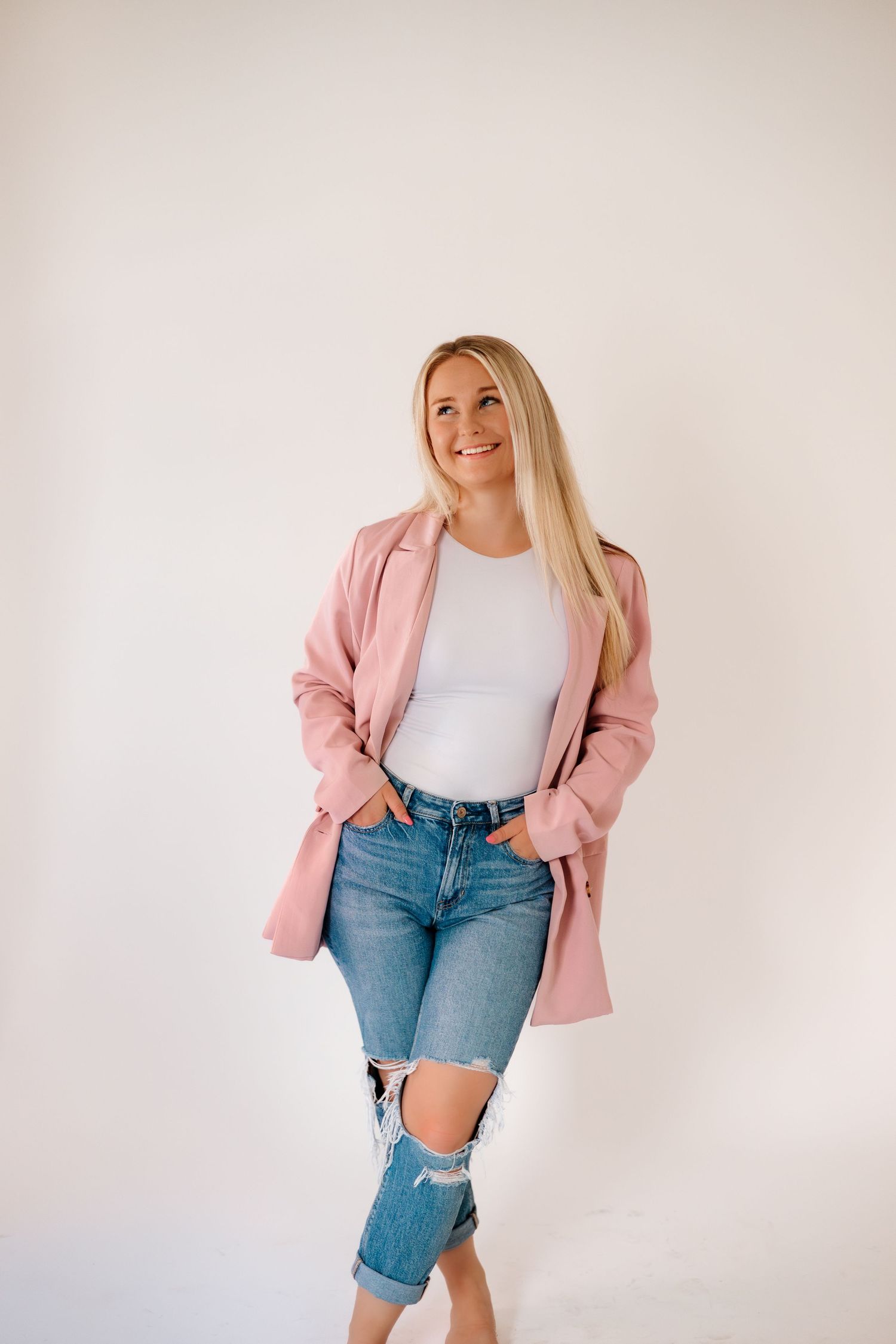Fashion photography featuring casual style with distressed jeans and pink blazer against white background.
