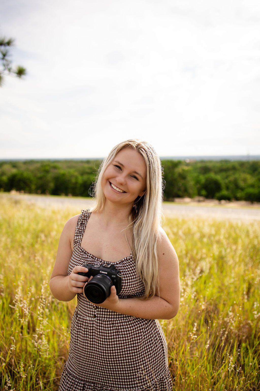 A photographer in a checkered dress captures moments in a sunlit summer meadow with wildflowers.