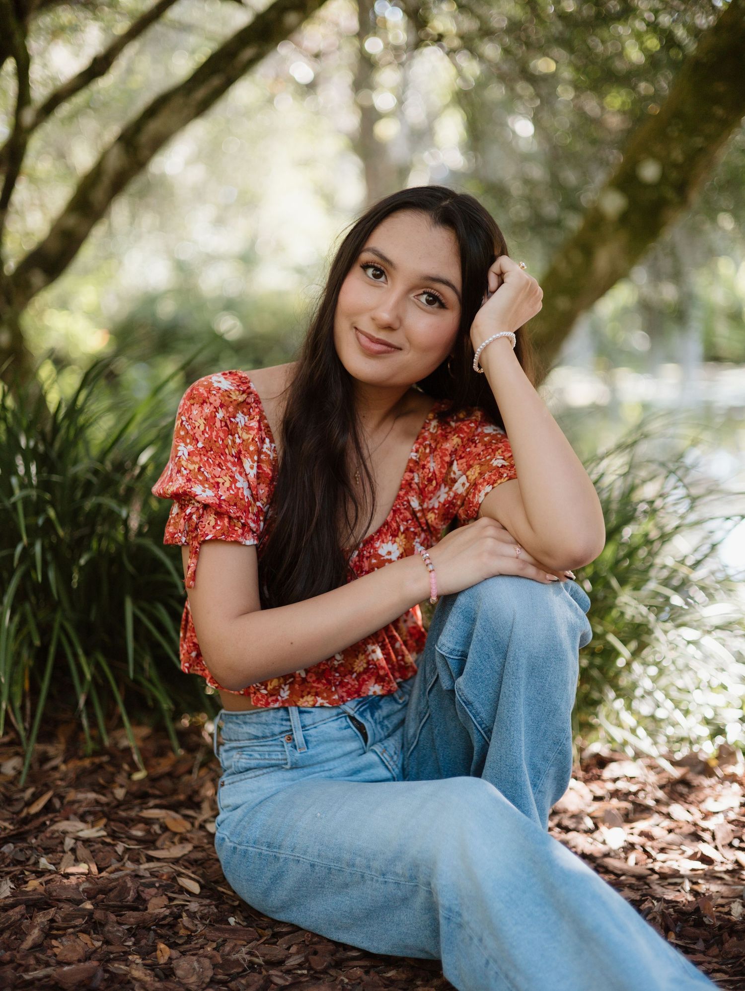 Casual portrait in red top and jeans sitting among garden foliage.