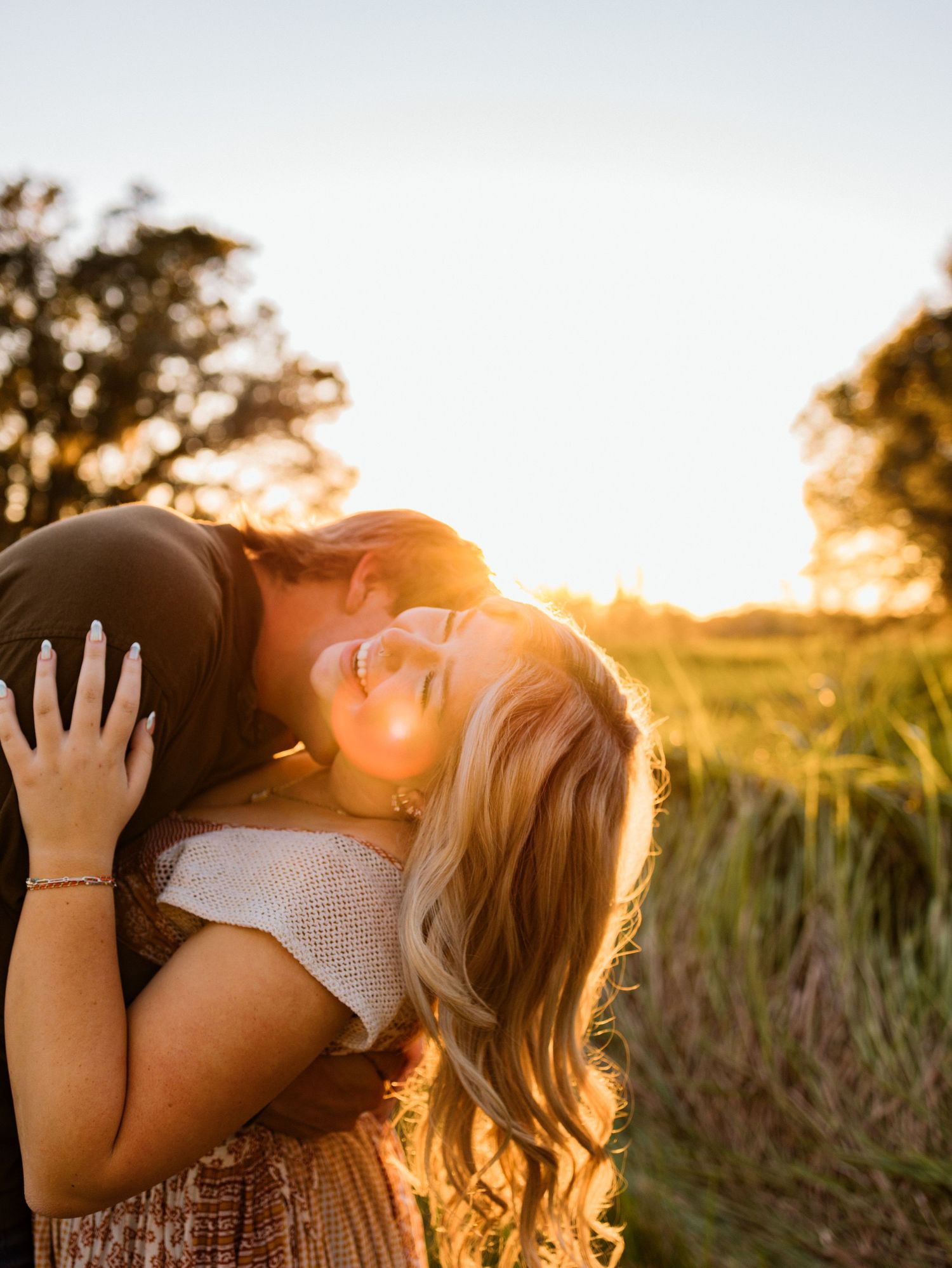 A tender embrace captured during golden hour in a field of tall grass with sunlight streaming through at sunset.