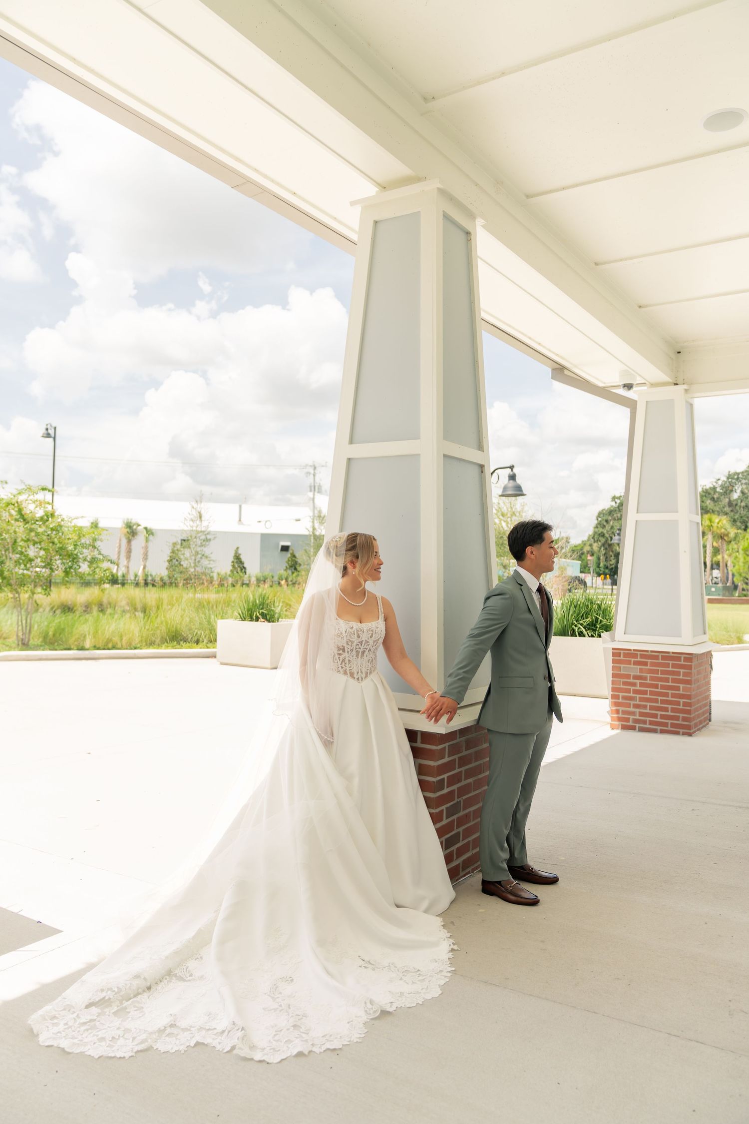 Bride and groom hold hands around a pillar during a romantic first look at an outdoor wedding venue.