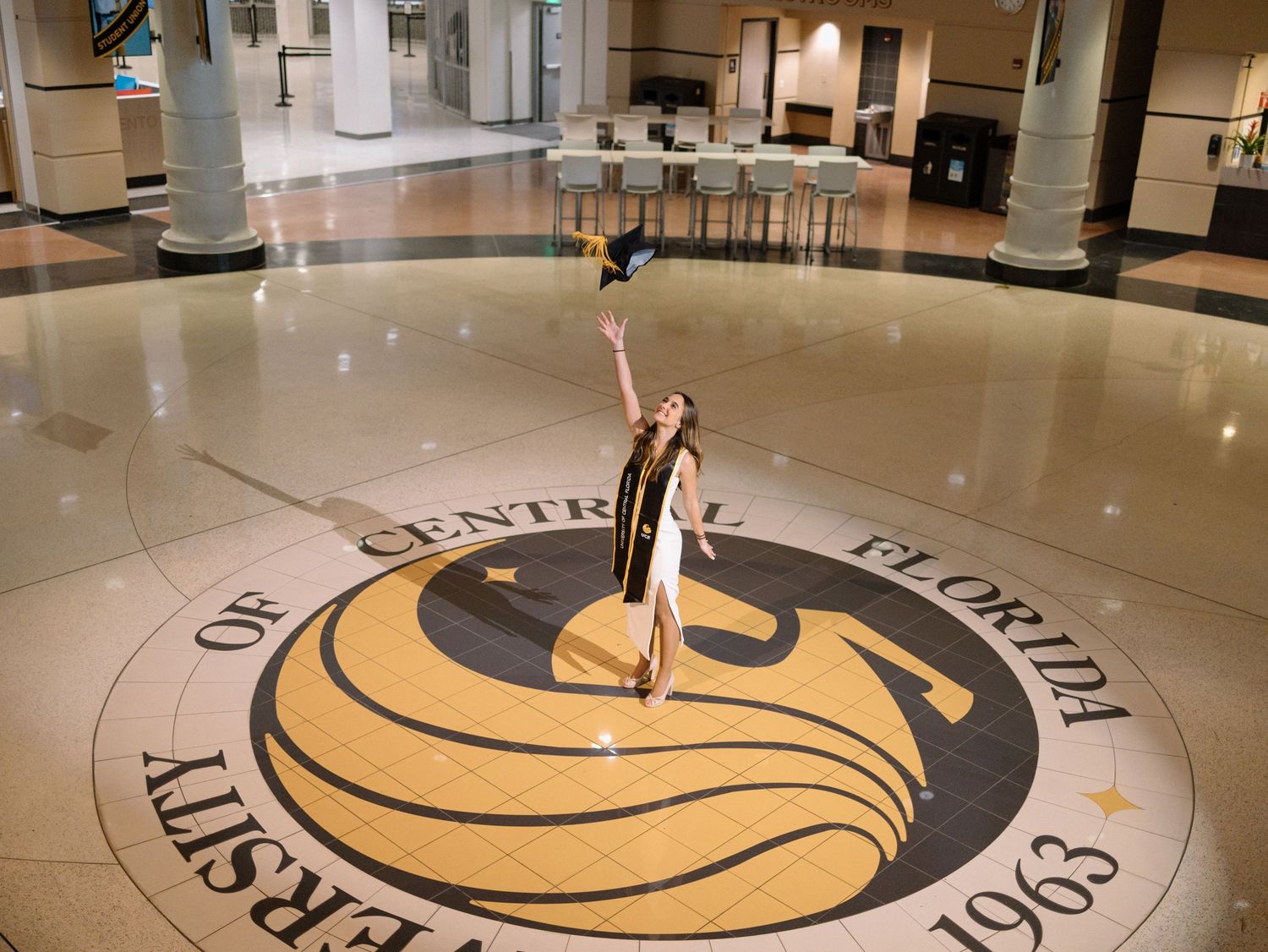 UCF graduate tosses cap above the University of Central Florida seal on the floor of a campus building.