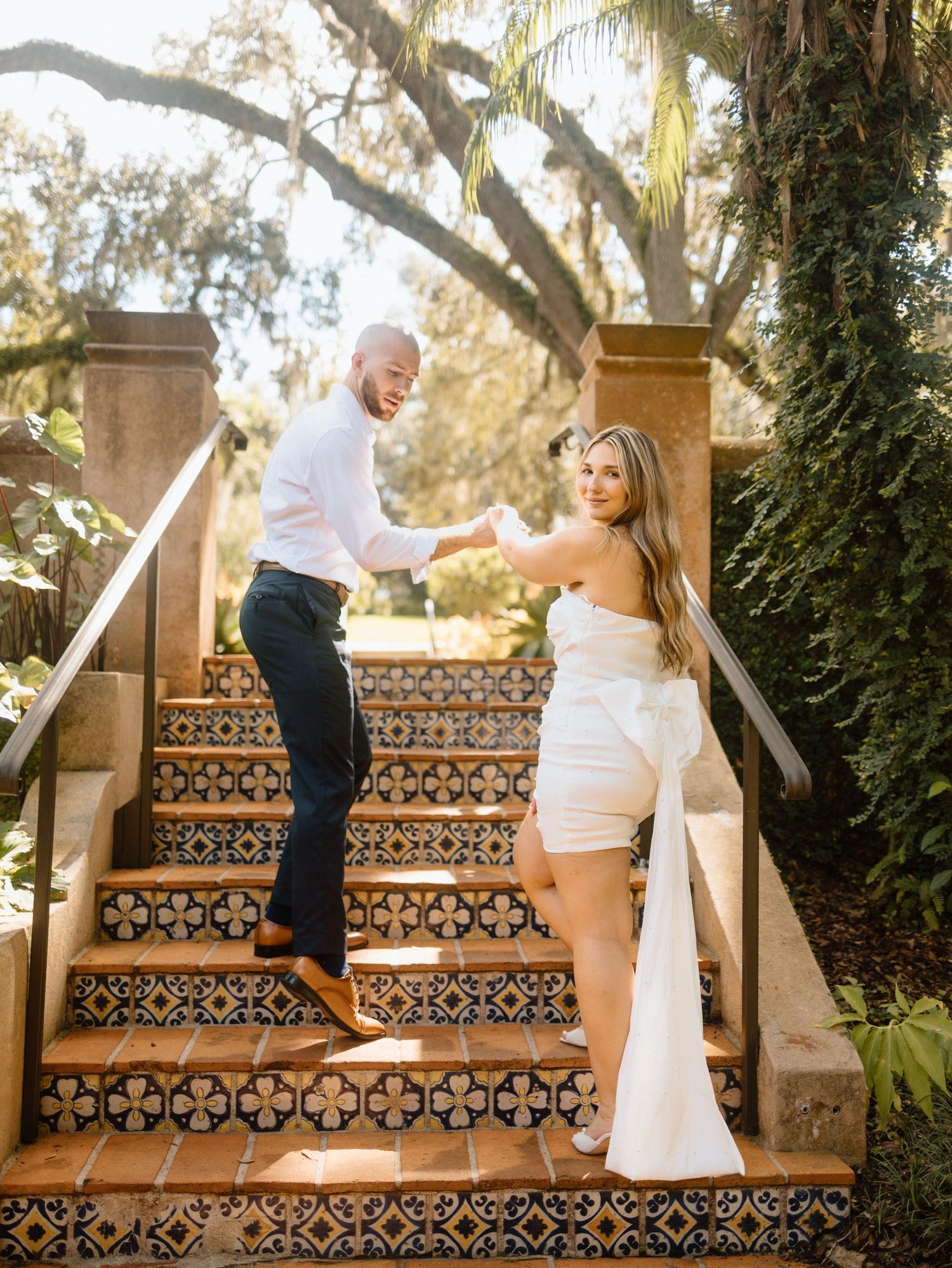 A couple poses on decorative tiled steps in a sunny garden setting.