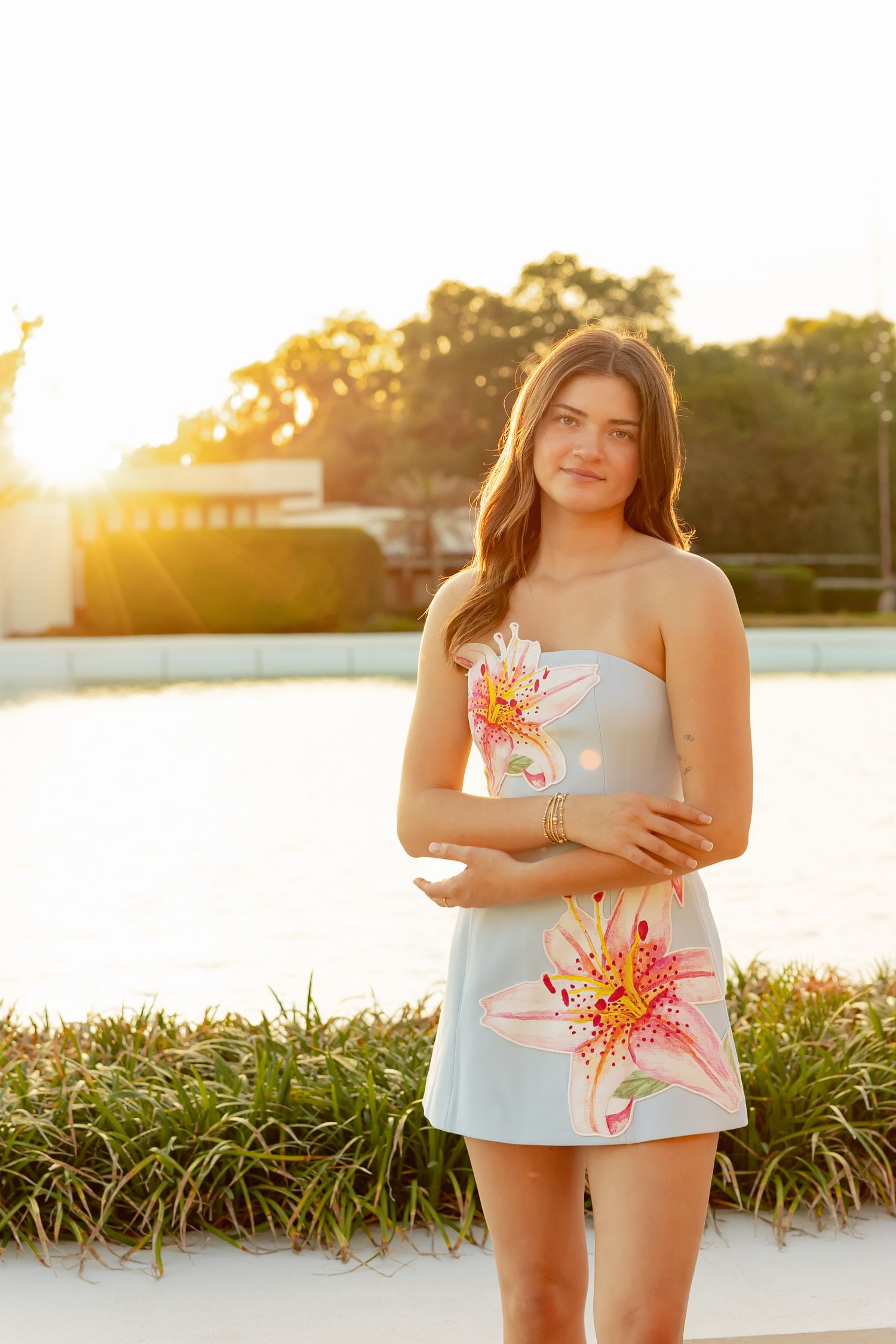Young woman in a floral strapless mini dress poses outdoors during a golden sunset photo session.