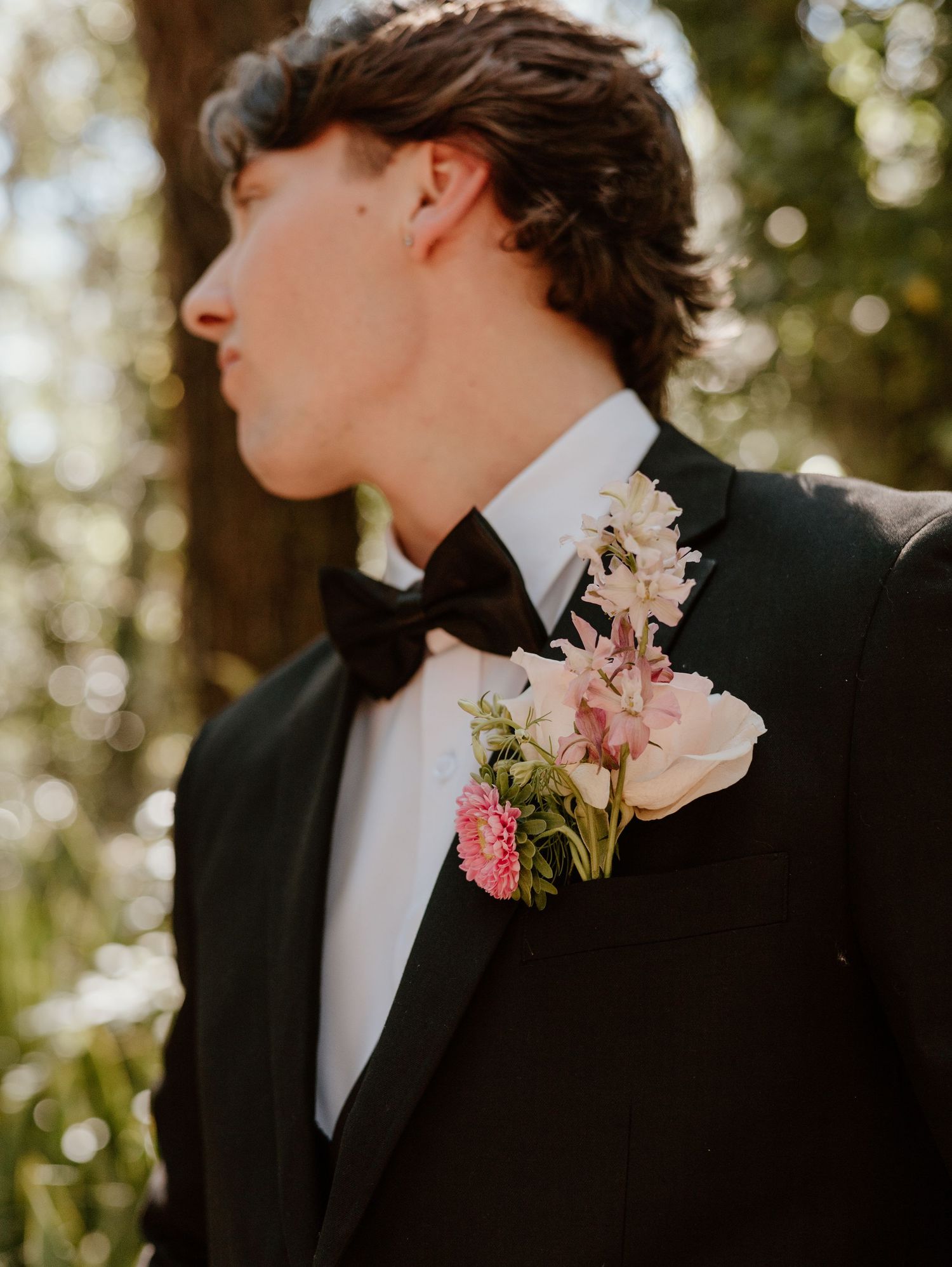 A close-up shot of a boutonniere with pink flowers on a black tuxedo lapel.