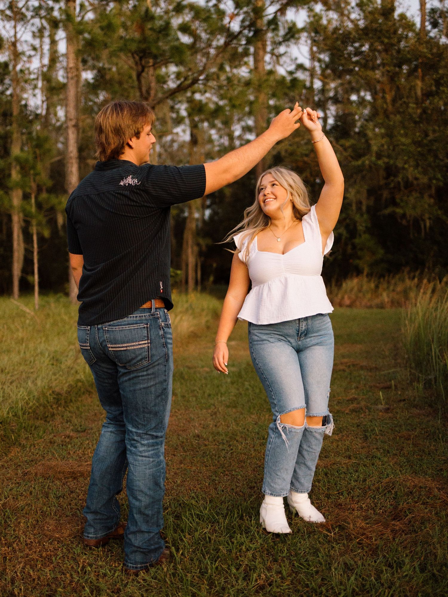 Couple dancing playfully in a wooded outdoor setting during golden hour, creating a joyful sequence of movement.