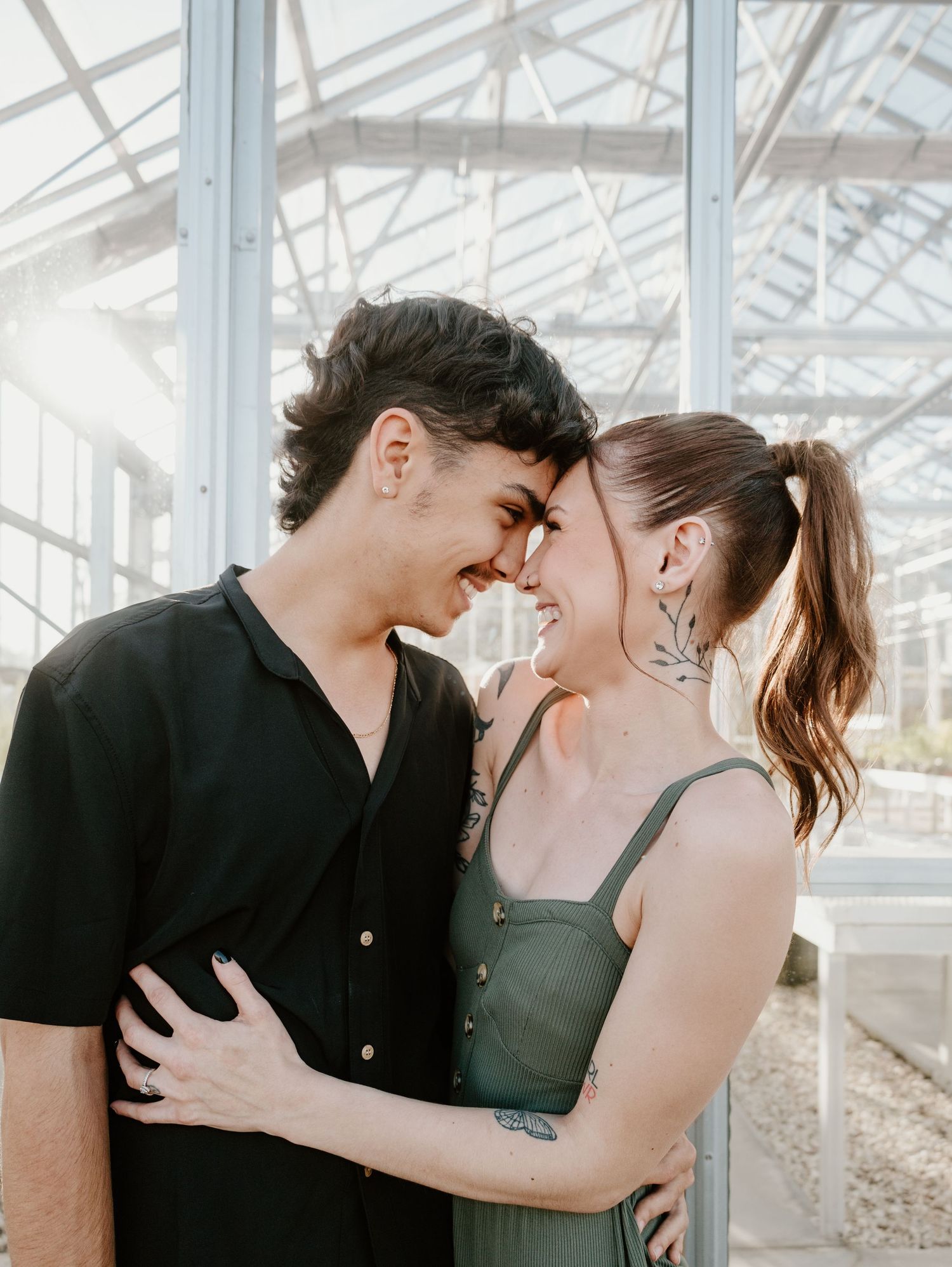 Intimate couple sharing a tender moment together in a bright greenhouse setting with natural lighting.