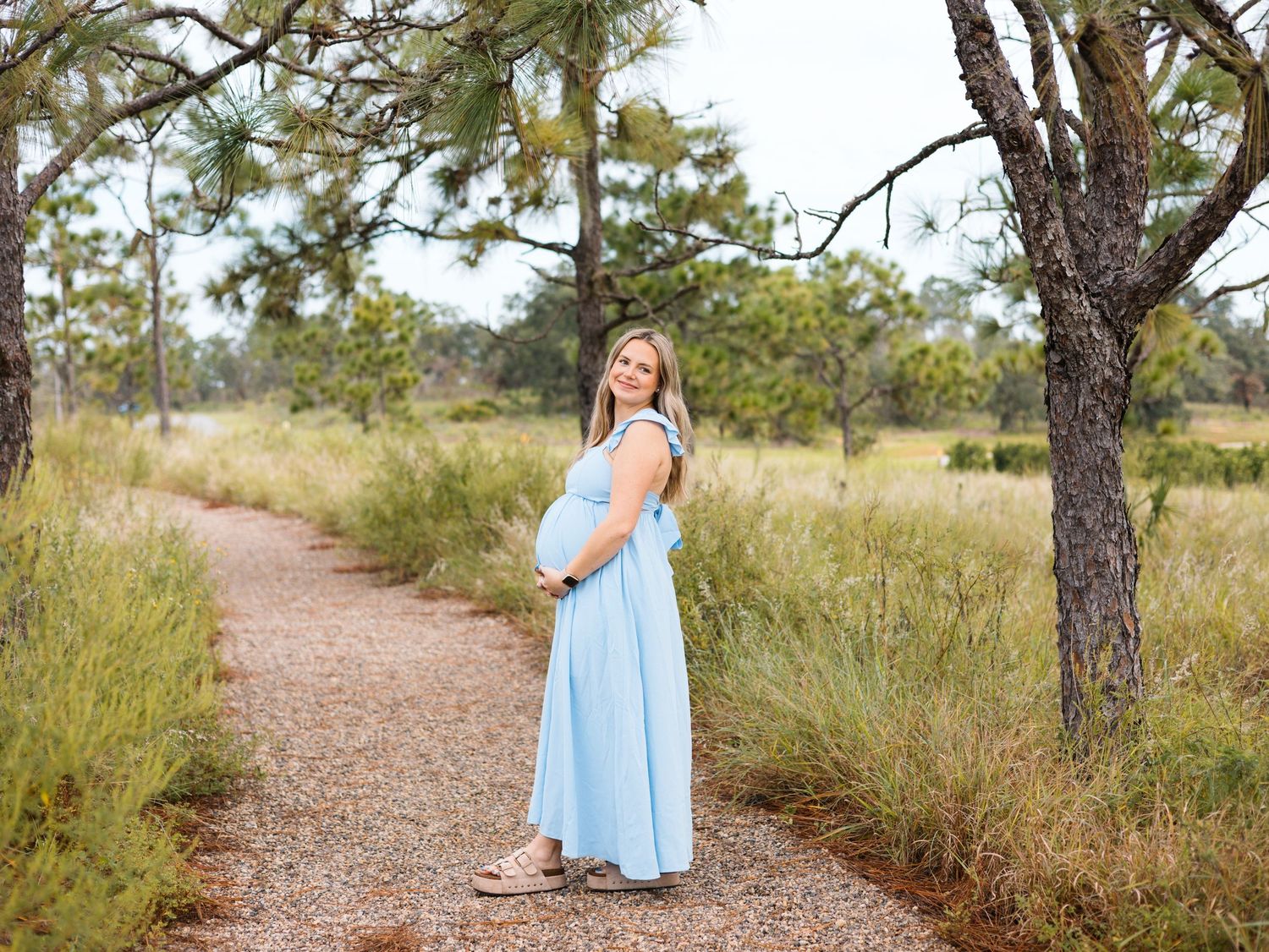 A light blue dress flows in the breeze along a winding dirt path through a serene natural landscape at sunset.