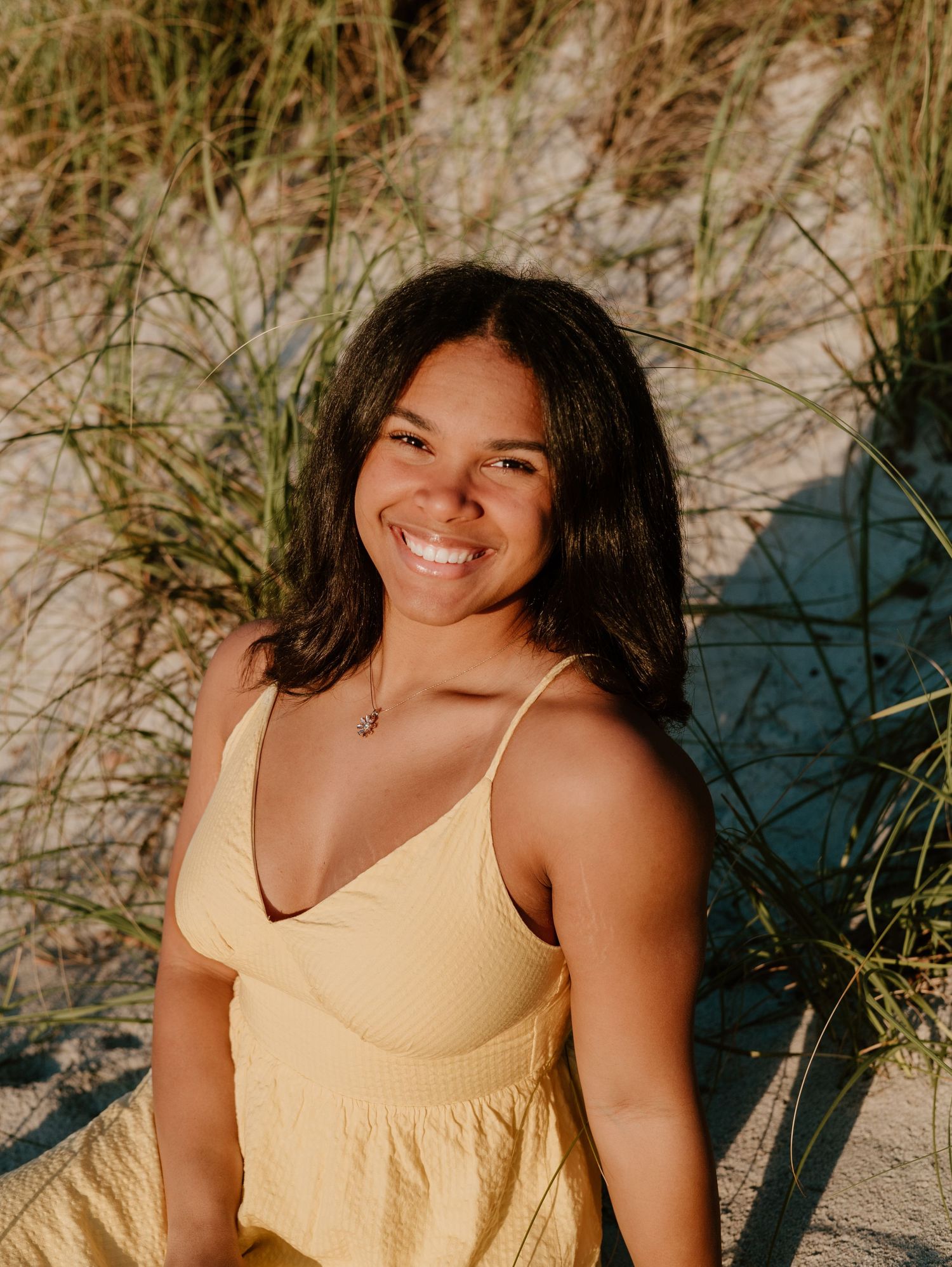 Woman in yellow sundress posing on beach with natural lighting.