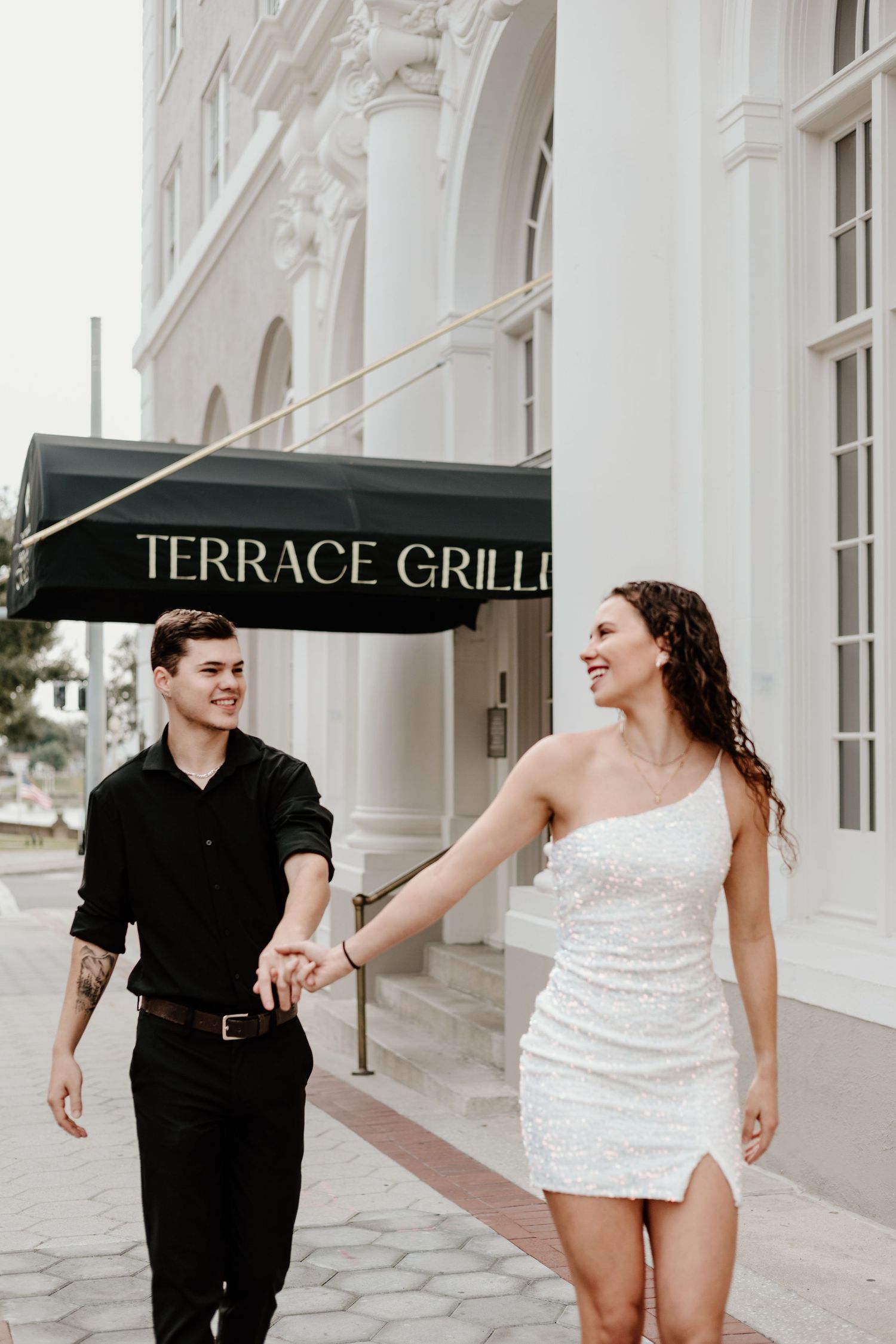 Couple running playfully outside Terrace Grill in formal attire.