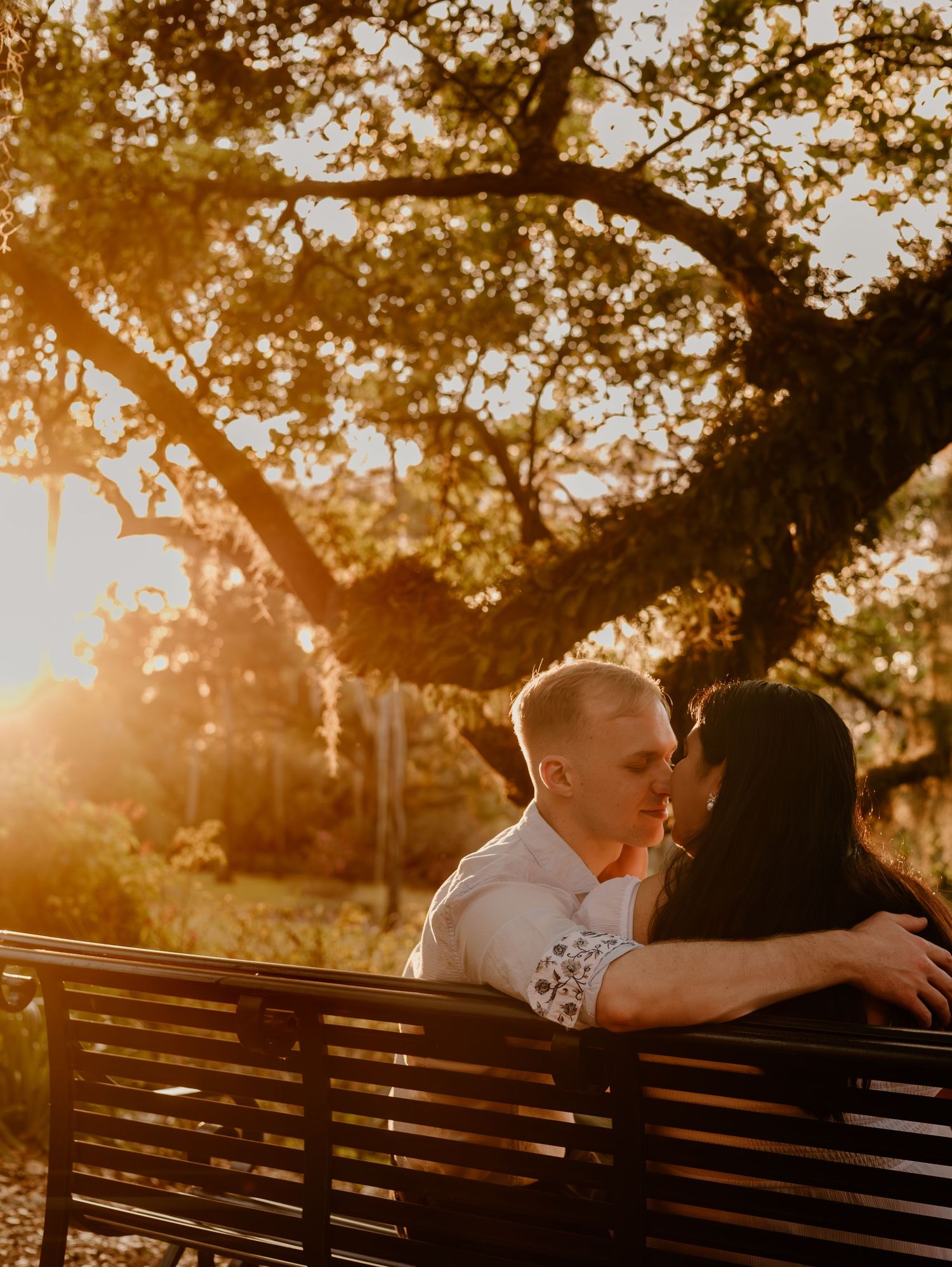 Couple sharing tender moment on wooden bench during golden sunset.