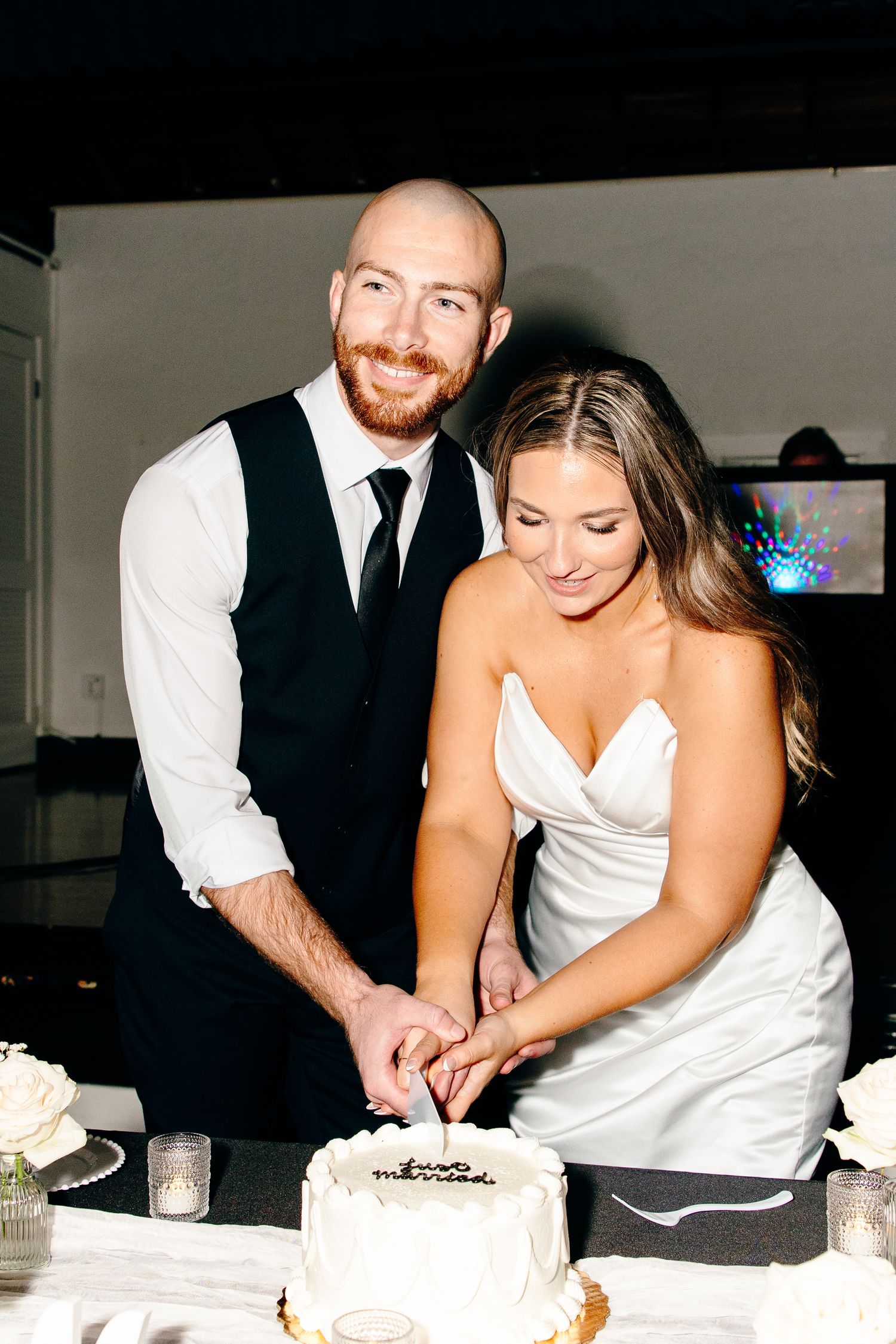 Smiling bride and groom cut their white wedding cake together at their indoor wedding reception.