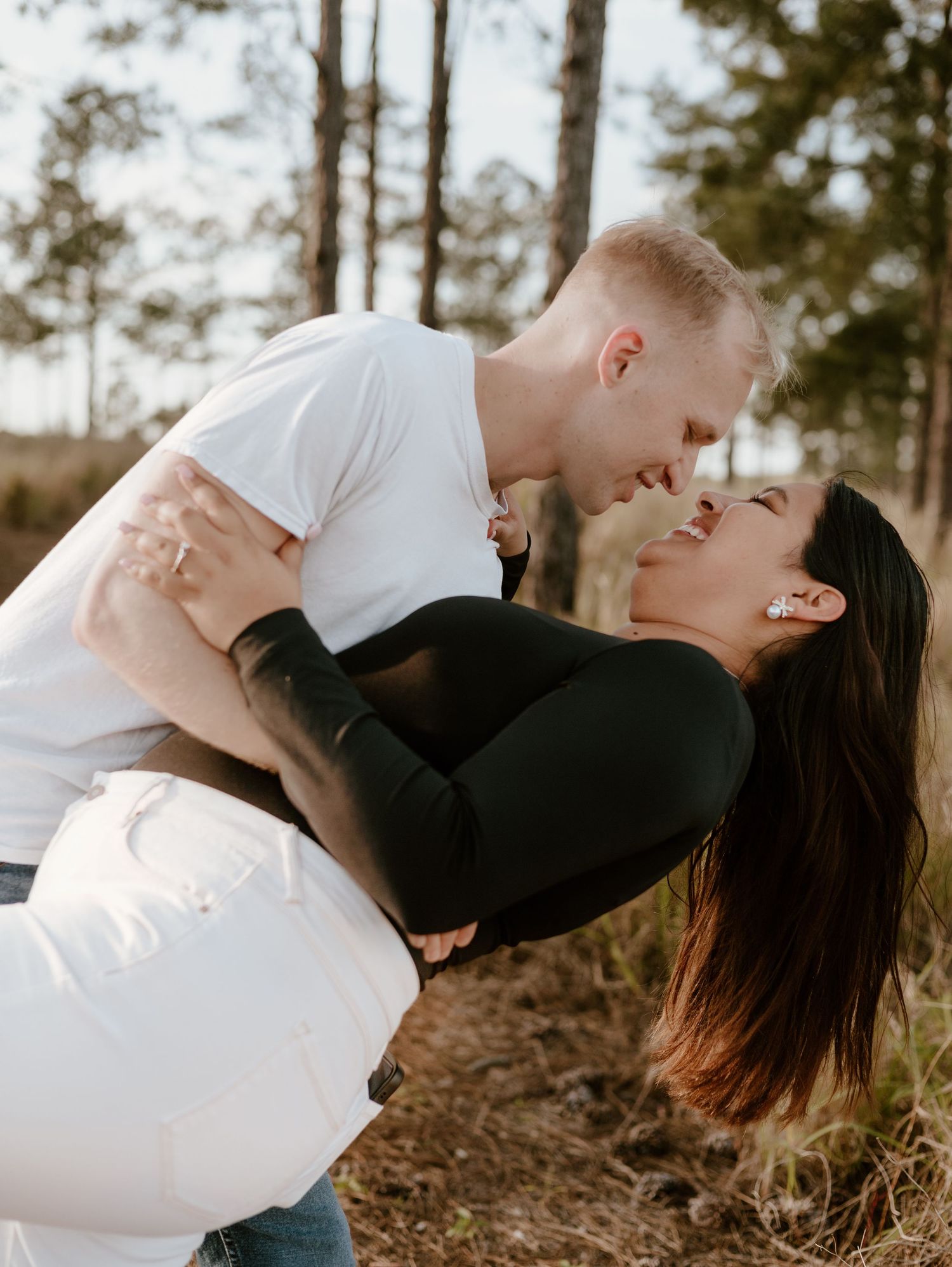 Romantic outdoor embrace against a forest backdrop during golden hour.