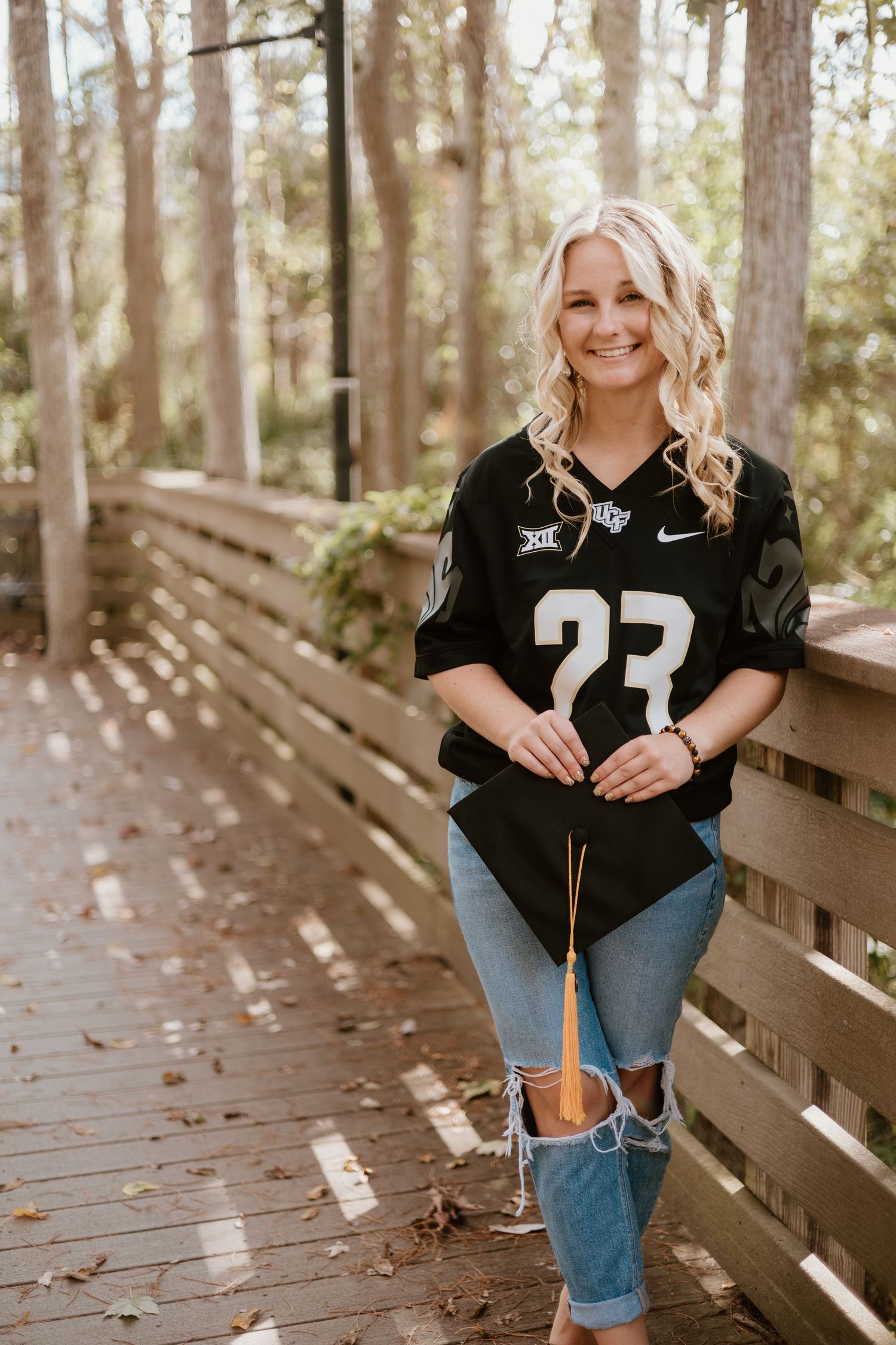 A series of graduation photos taken on a wooden boardwalk in a forest setting showing someone in a black jersey.
