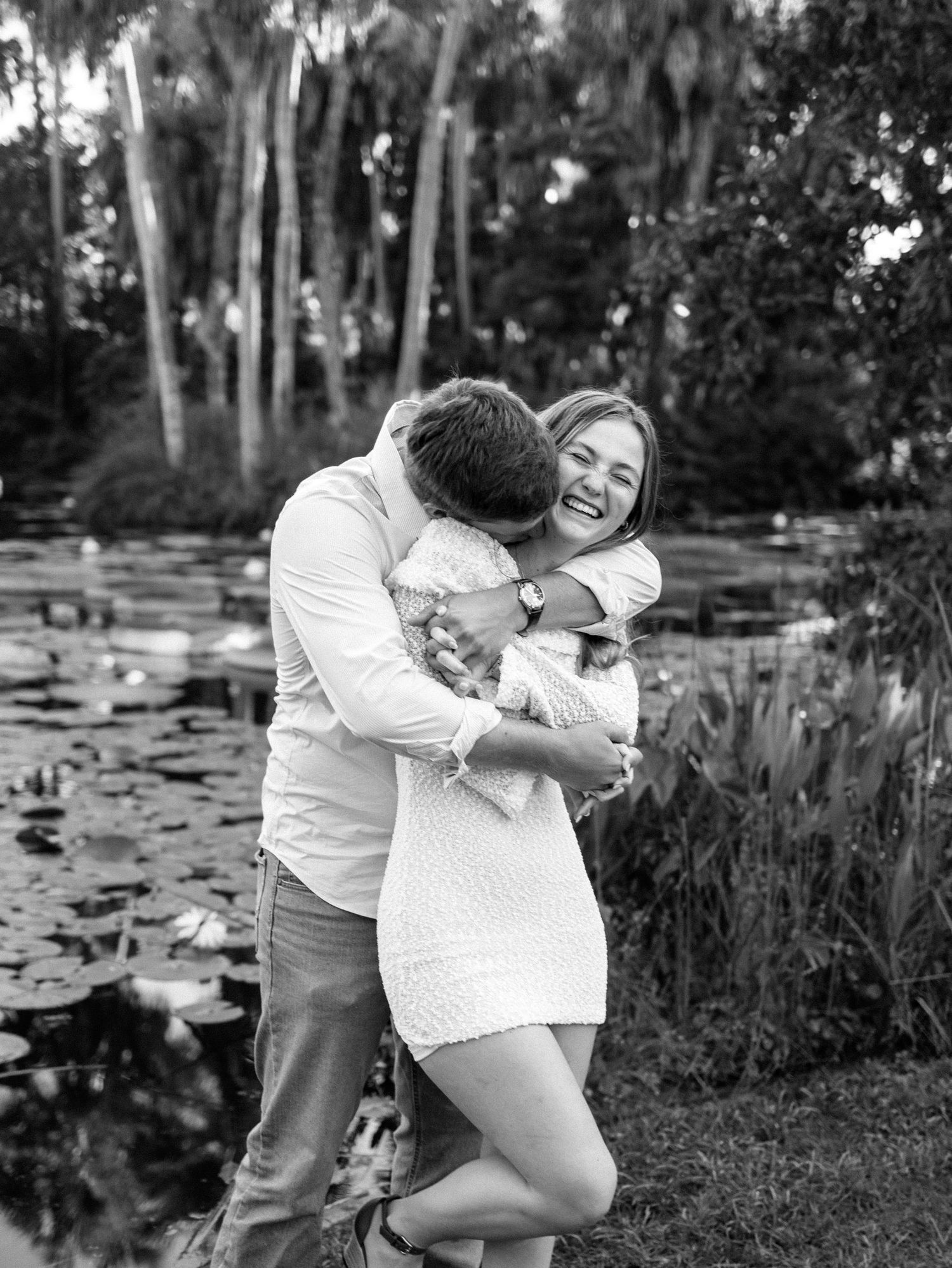 A romantic couple shares tender moments by a serene lily pond in a natural outdoor setting.