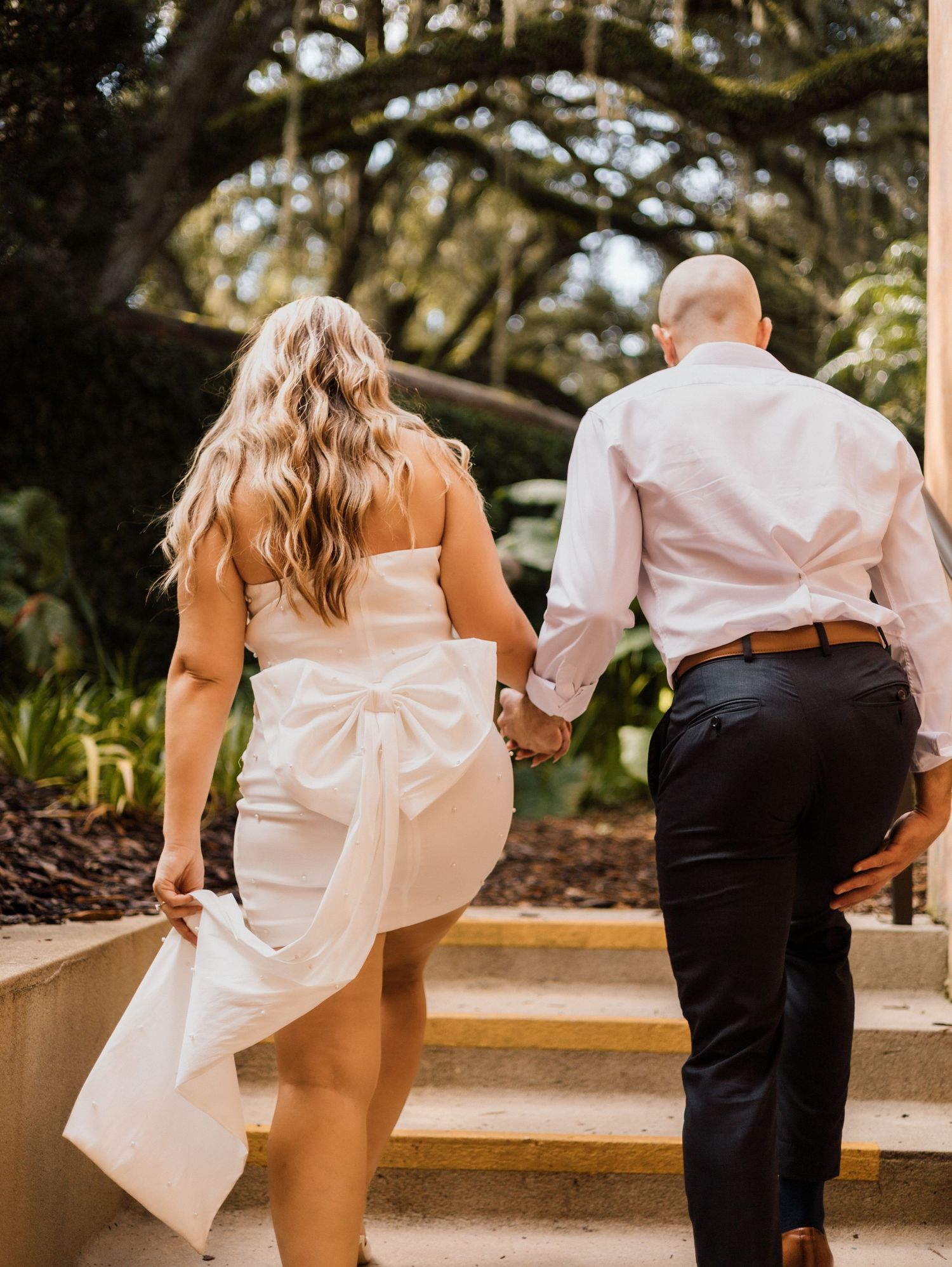 A playful couple in wedding attire shows off their fun side with matching poses in an outdoor garden setting.