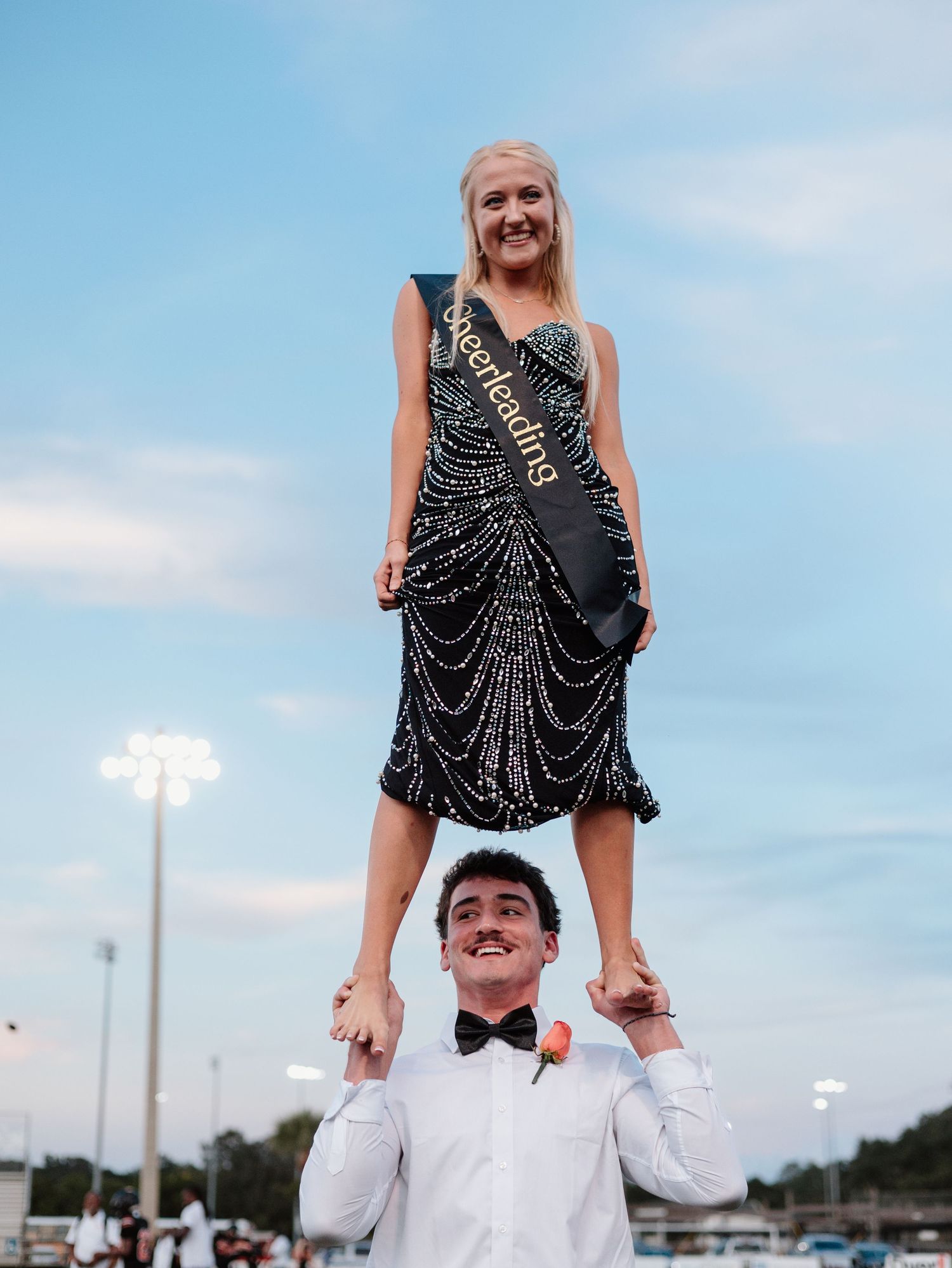 A couple performs an impressive acrobatic stunt with one person standing on the other's shoulders in formal attire.