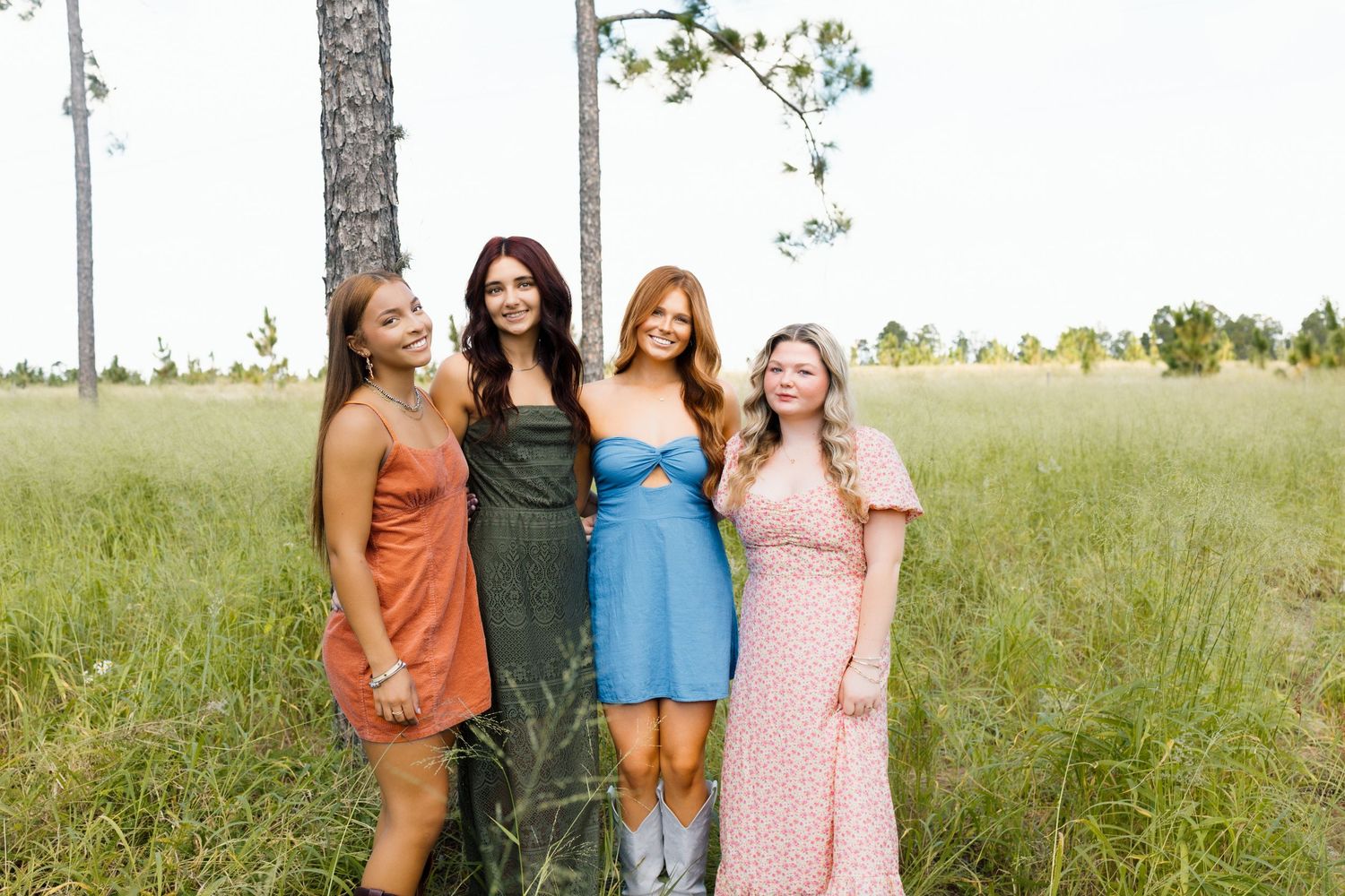 A group stands together in a grassy field on a bright summer day wearing colorful casual dresses.