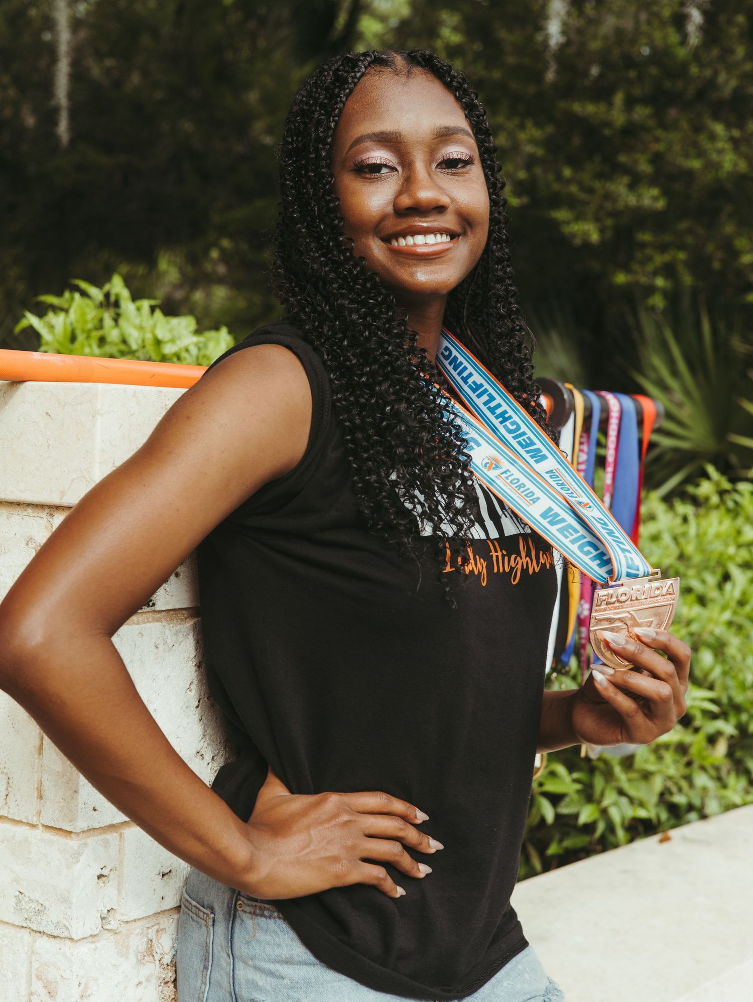 Graduate holding diploma and posing in black gown outdoors.